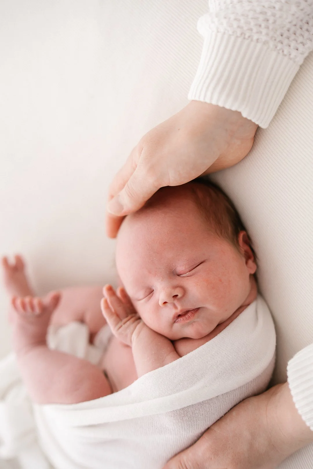 Vauva nukkuu vanhemman sylissä, mutta käsi koskettaa hänen päätään.