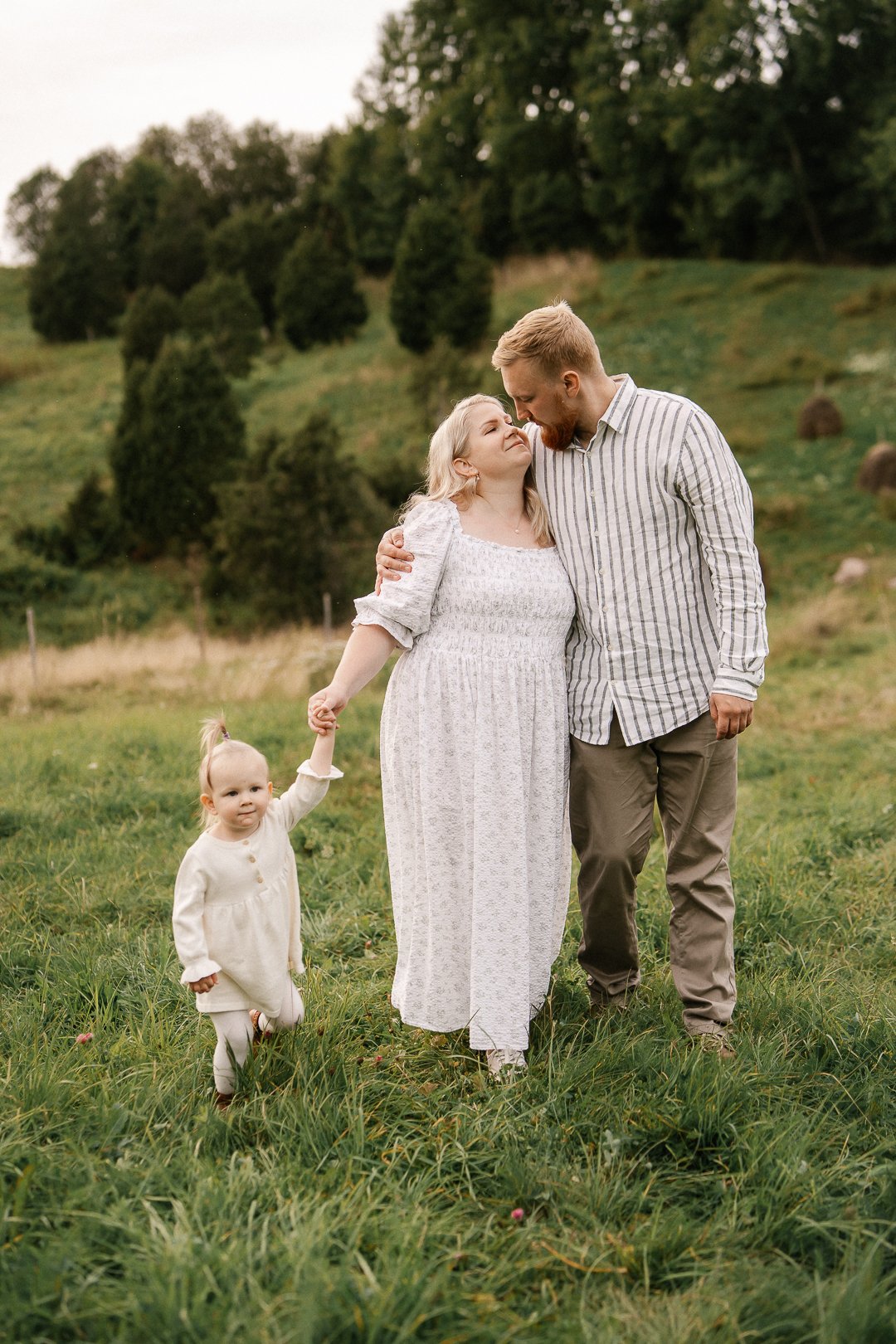 Perhe kävelee rinteessä, jossa on vihreitä puita ja kukkalehtiä, hyvässä säässä.