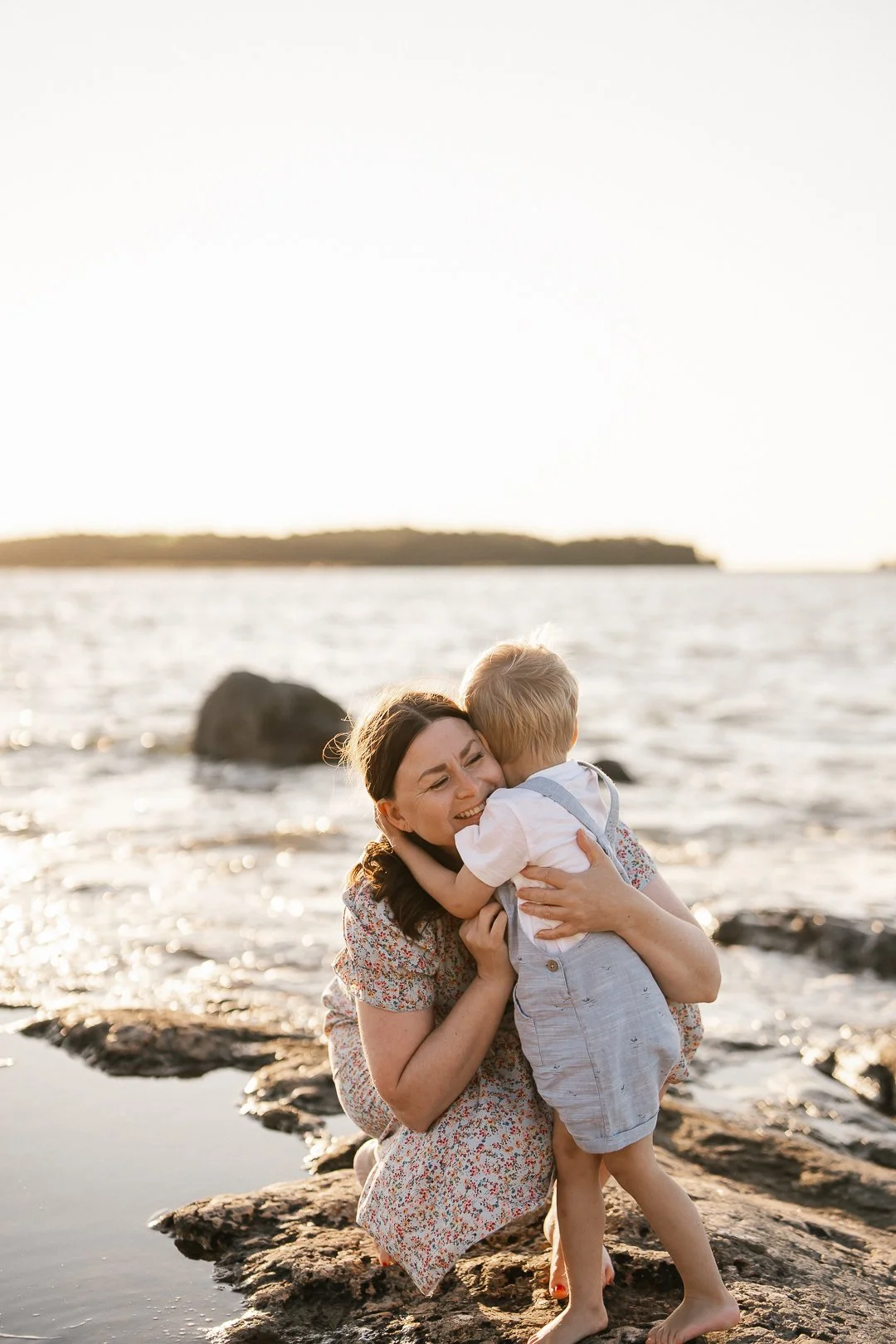Äiti ja lapsi halaavat rannalla auringonlaskun aikaan.