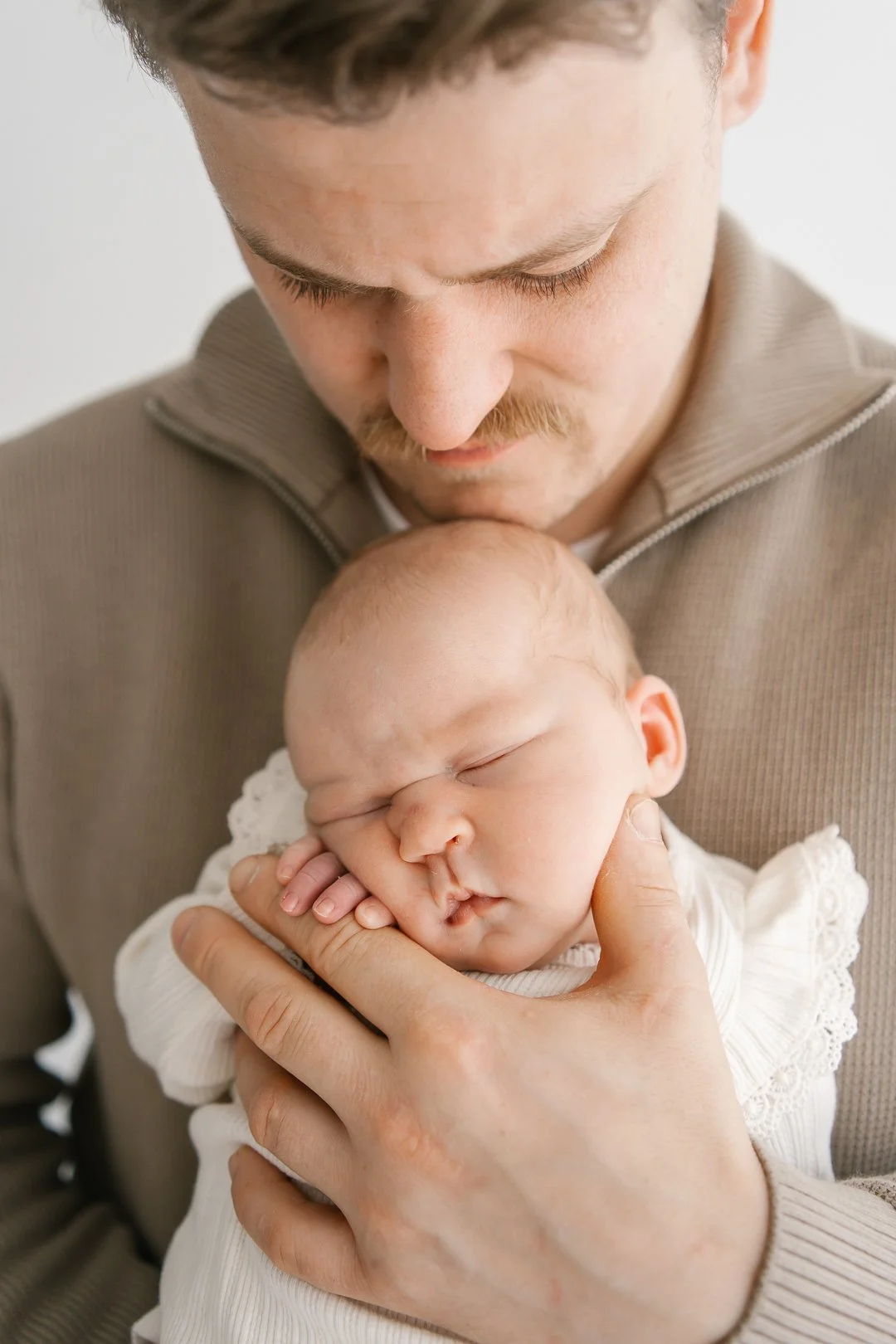 Mies pitää pientä nukkuvaa vauvaa rinnallaan, katsoo hellästi vauvaa.