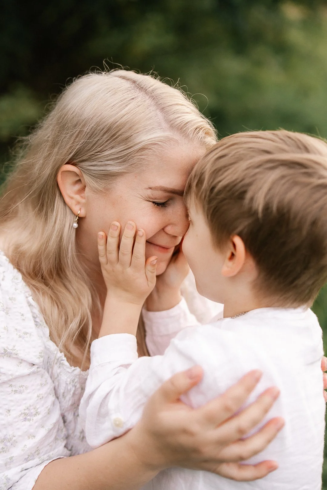 Lapsi ja nainen halaavat ja koskettavat otsaa toisilleen luonnossa, onnellinen hetki.
