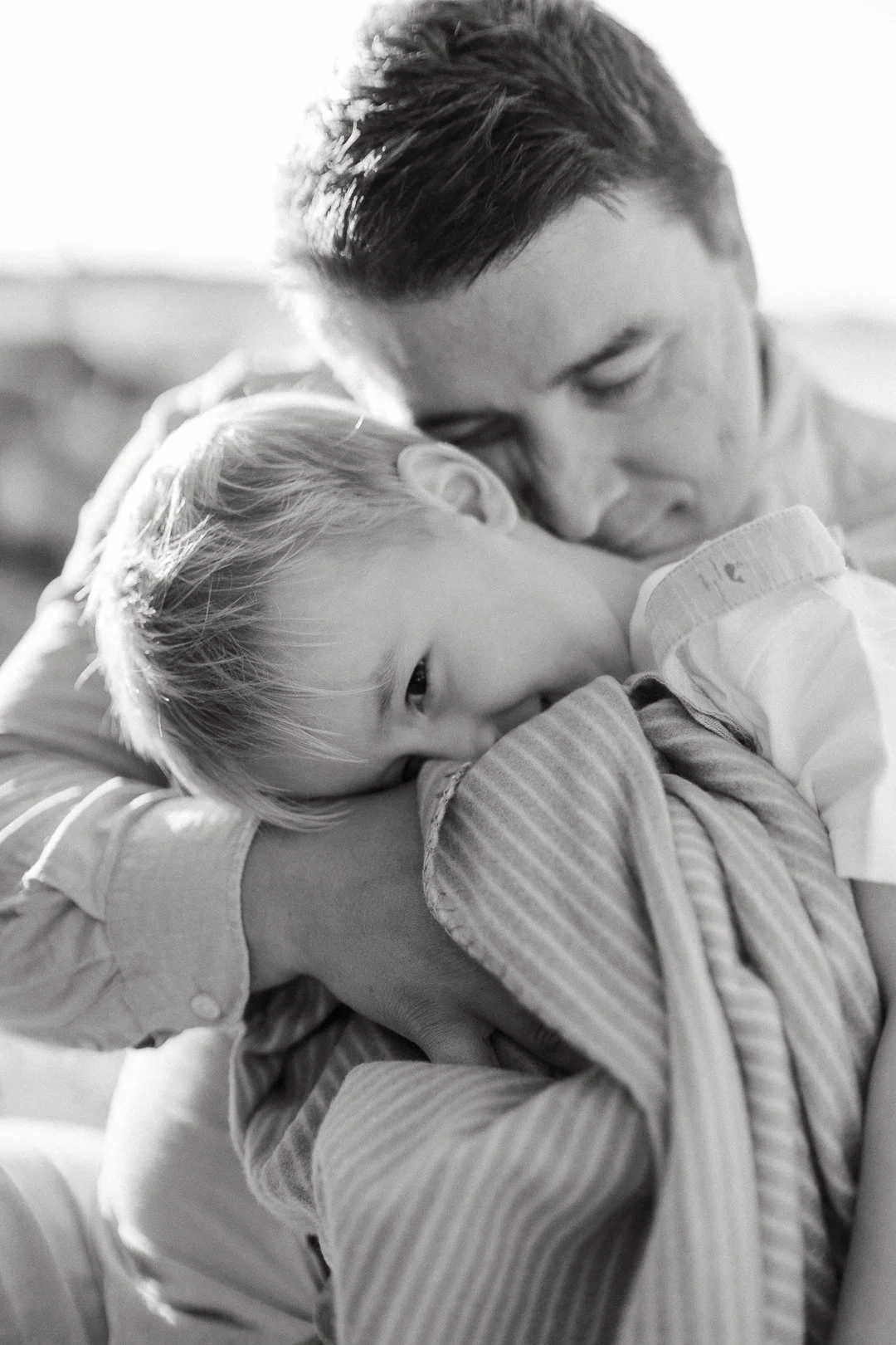 Mustavalkoinen valokuva isästä ja lapsesta halaamassa, lapsi nukkuu ja katsoo kuvaan.