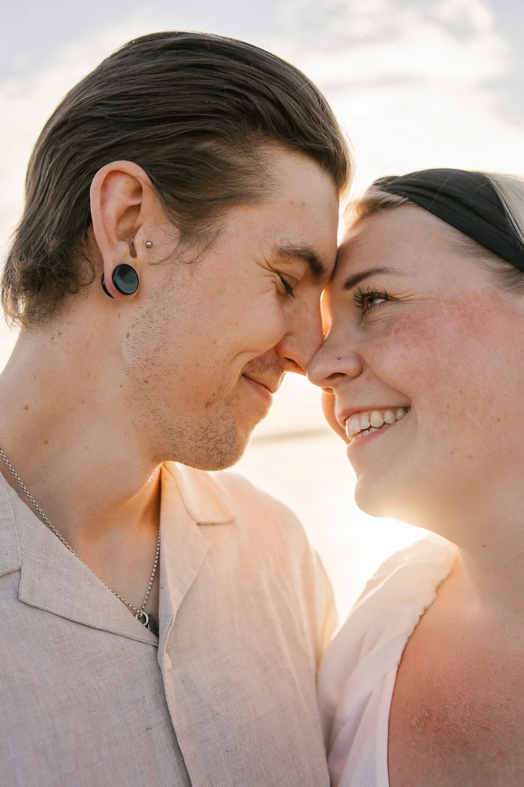 Kaksi ihmistä koskettavat otsiaan ja nauravat lähekkäin ulkona auringonlaskussa.