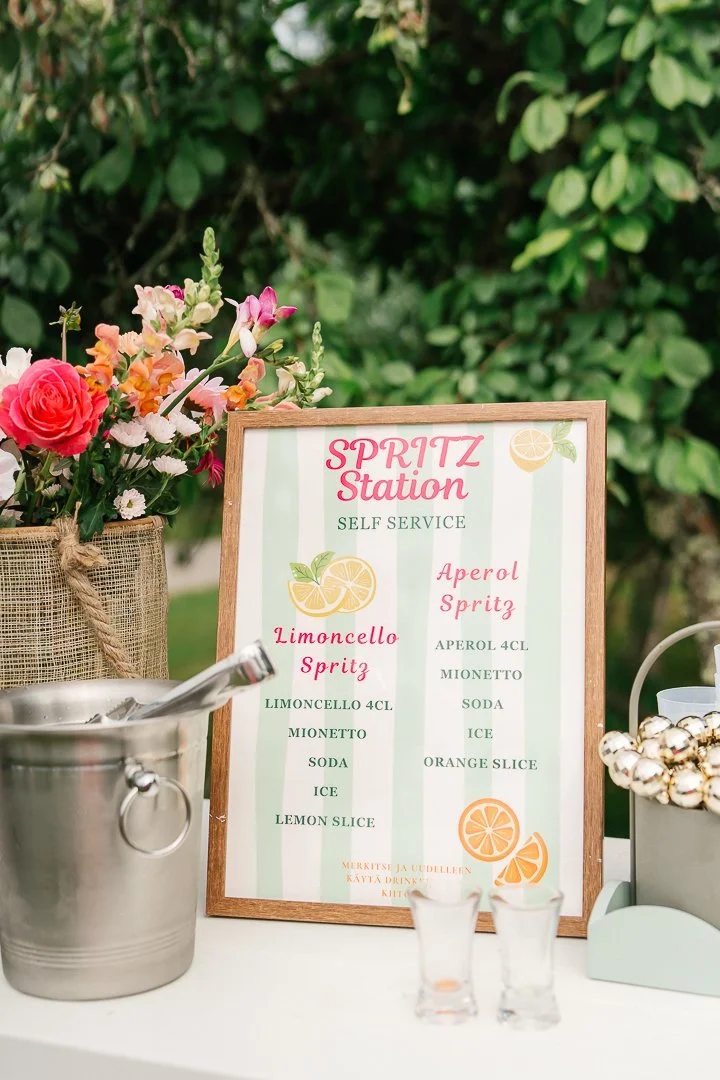 Kuva spritz-juomien itsepalvelupisteestä, jossa on tarjoilulista ja kukkakimppu.
