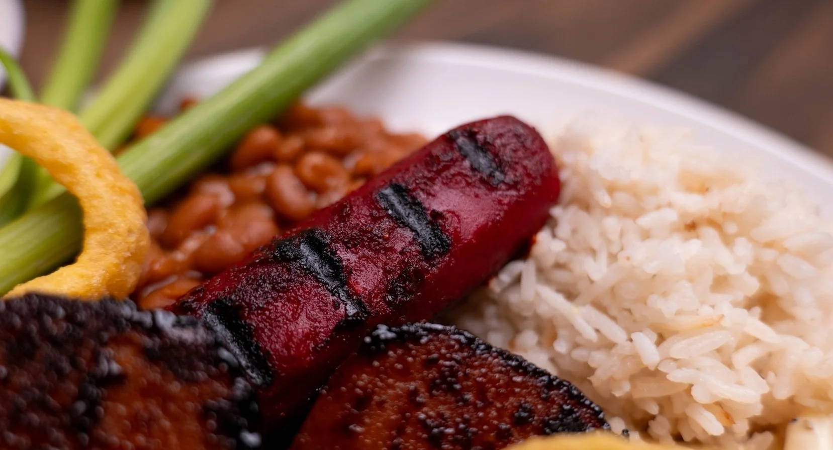 Red dog on a plated lunch with rice and baked bean.