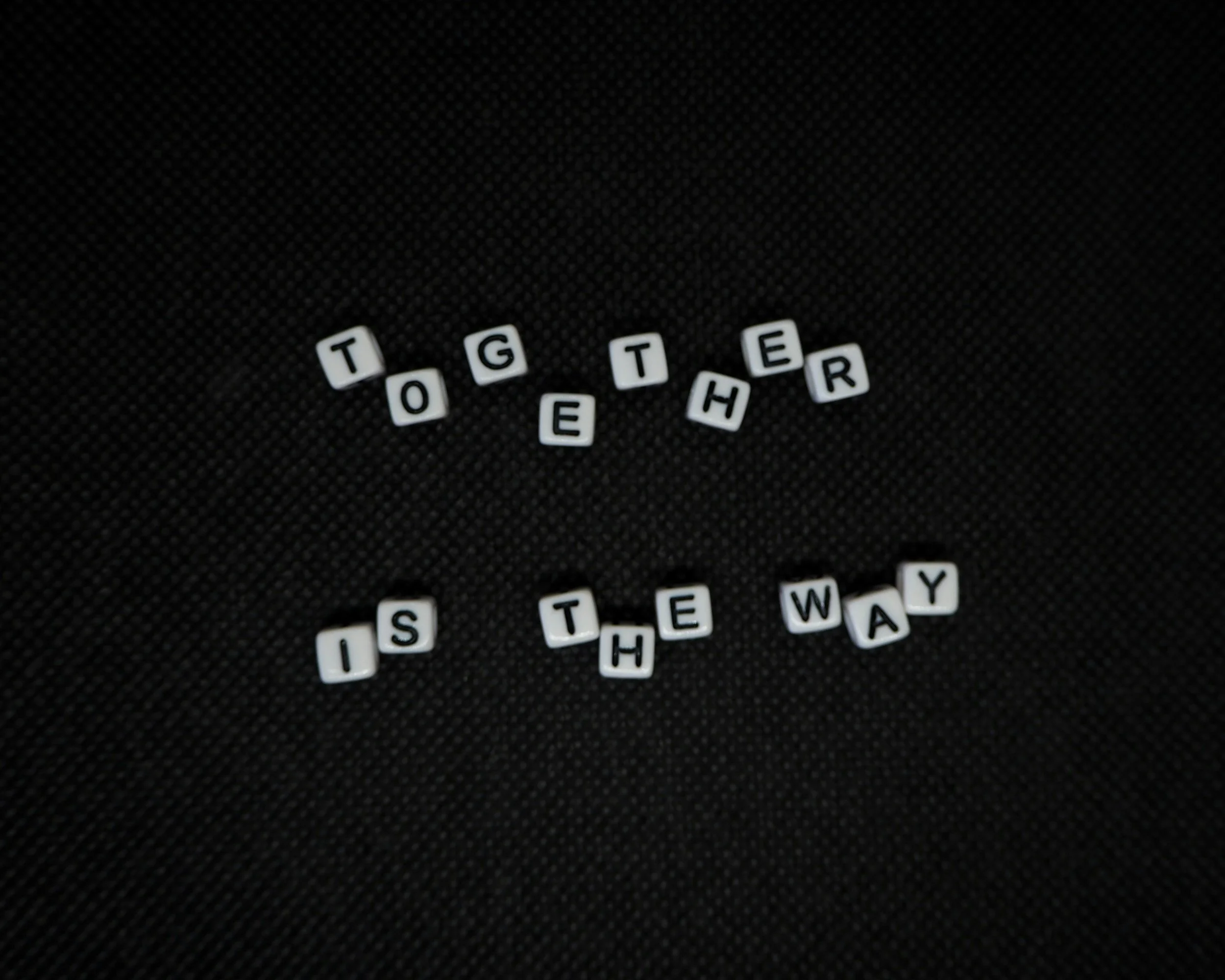 Letter beads spelling out 'Tougher is the way' on black textured surface.