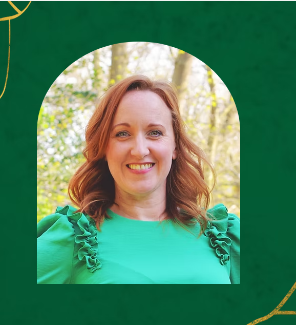 A smiling woman with shoulder-length auburn hair wearing a green top with ruffled shoulders, photographed outdoors with trees and soft natural light in the background.