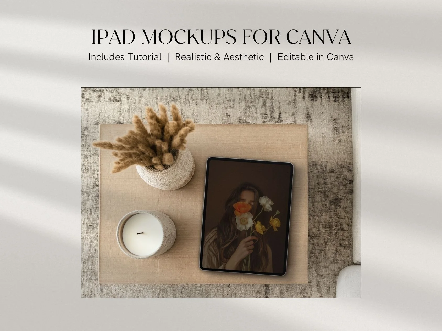 Top view of a flat lay arrangement on a light-colored surface including a tablet displaying a woman holding flowers, a small white candle, and a textured vase with dried pampas grass.