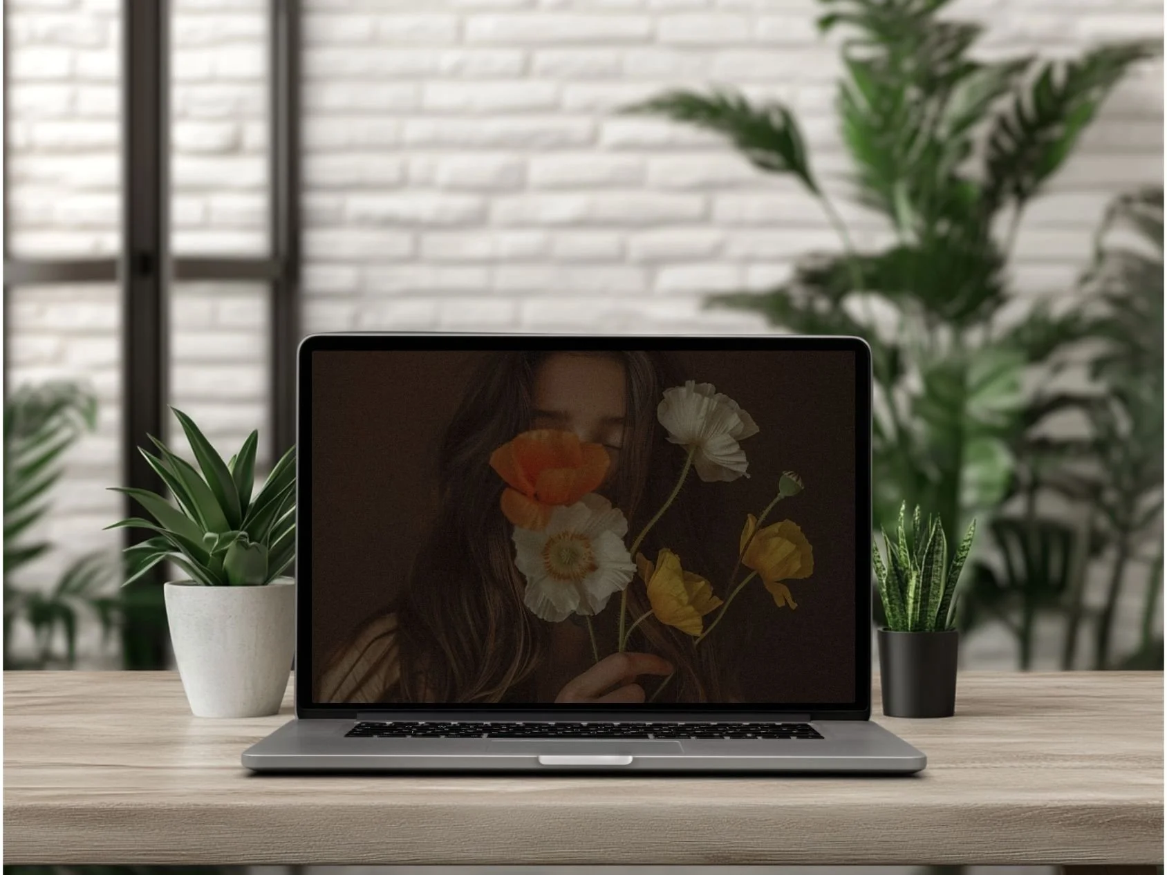 A laptop on a wooden desk with potted plants on either side, and a brick wall in the background.