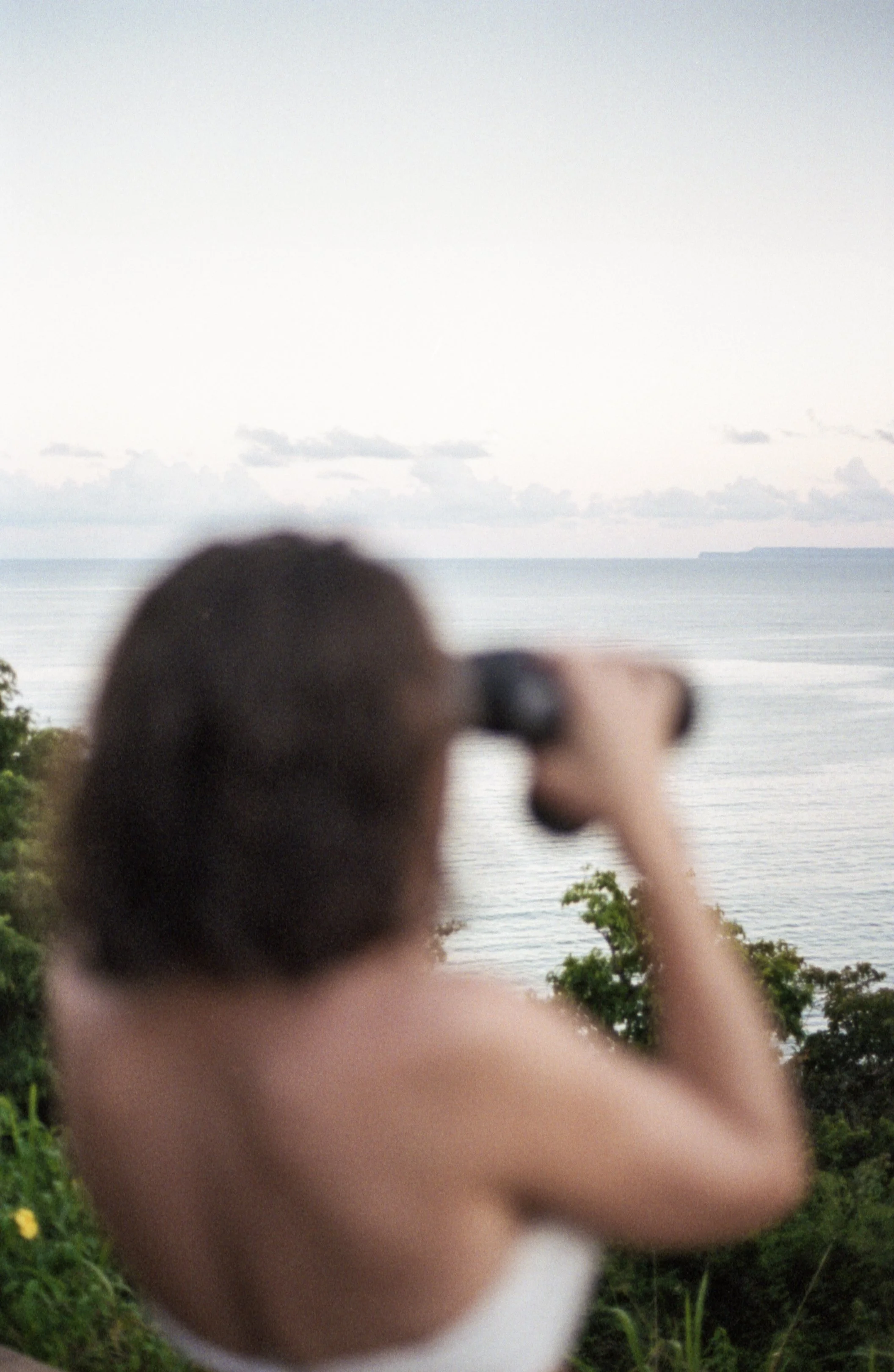 Personne avec jumelles regardant l'océan depuis un point de vue élevé avec végétation.