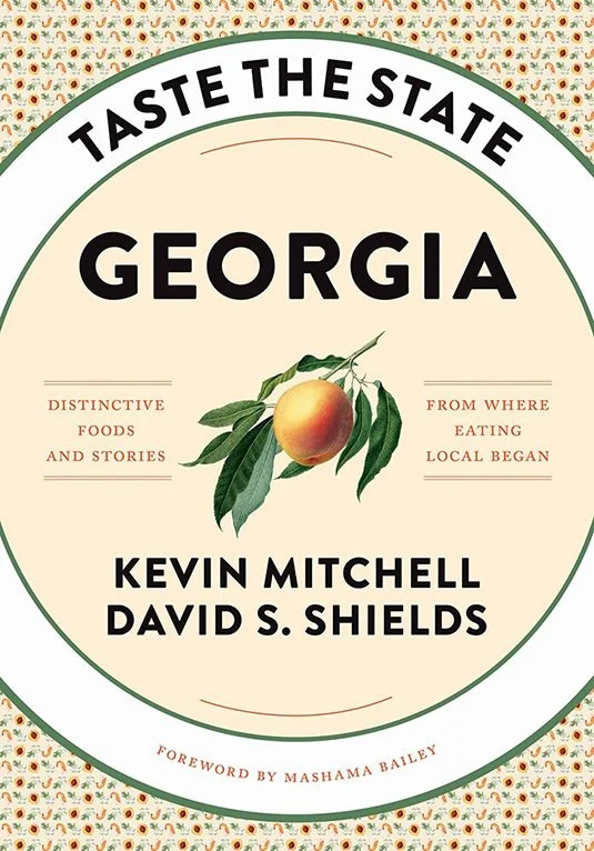 Book cover titled 'Taste the State Georgia' featuring a peach illustration, with authors Kevin Mitchell and David S. Shields, and a decorative border.