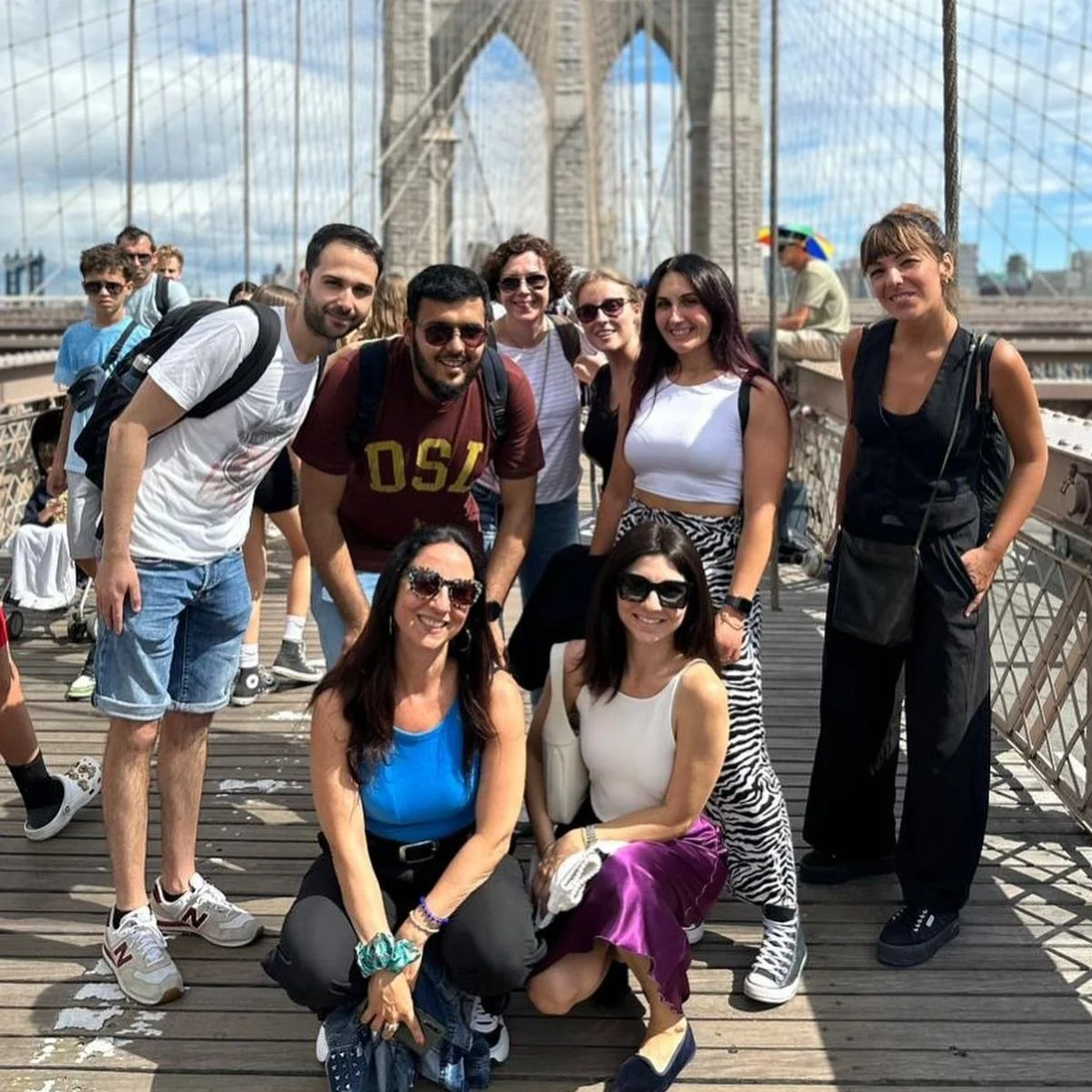 Group of people posing on the Brooklyn Bridge in New York City during daytime.