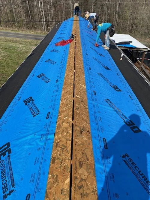 Construction workers installing roofing underlayment on a roof with a view of the surrounding trees.