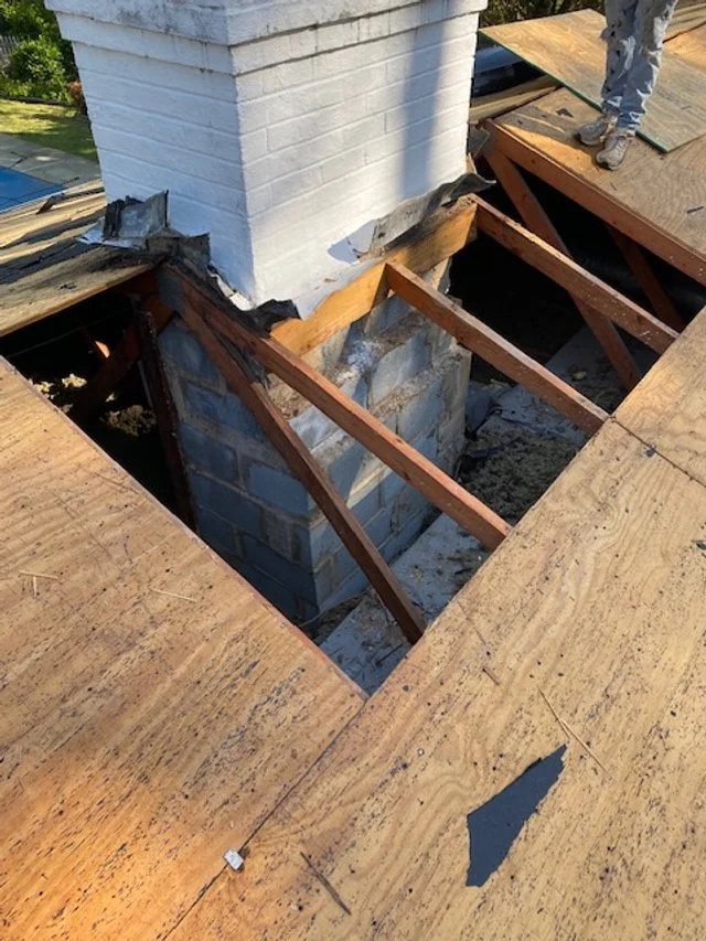 Construction site showing a chimney with unfinished wooden framing around the foundation of a roof.
