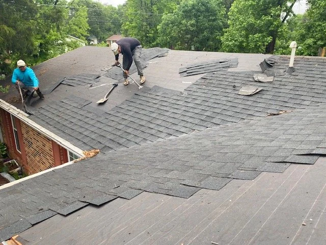 Two workers repairing a shingled roof, replacing damaged shingles.
