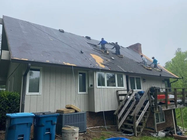 Multiple workers on a roof replacing or repairing shingles on a two-story house.