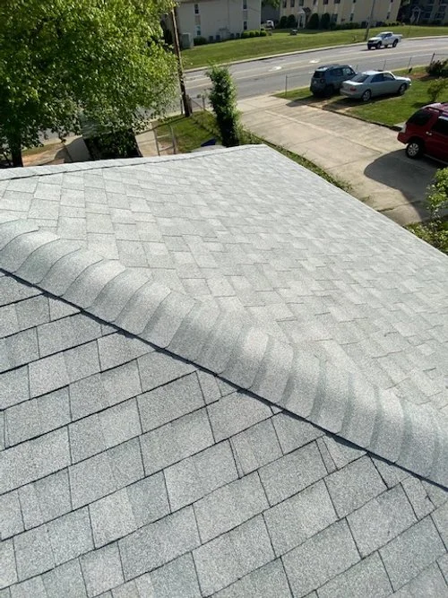 Close-up of gray shingle roof on a house with a clear sky and a street with cars in the background.