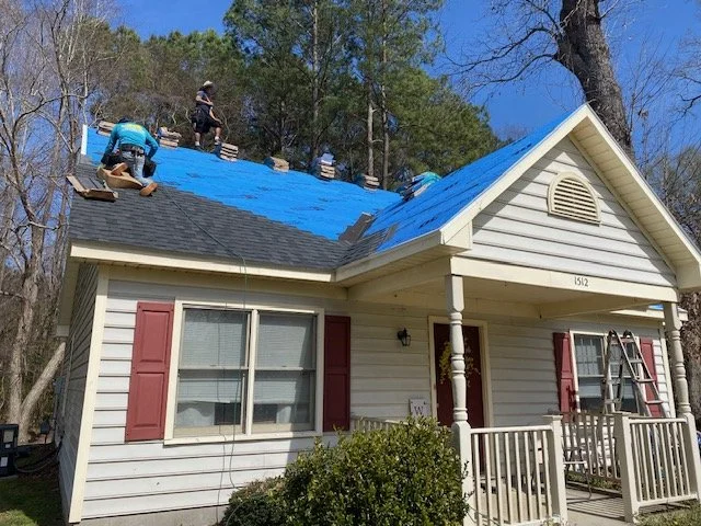 People installing bright blue roofing material on the house's roof during daytime.