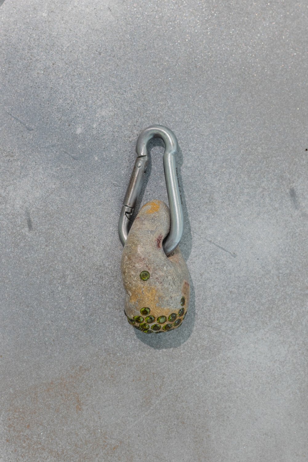 Darja Popolitova, Trouser pendant, 2026, Baltic Sea polished stone with hole, carabiner, laser engraving, lab-grown crystals, primitive shine. Photo: Kristīne Madjare