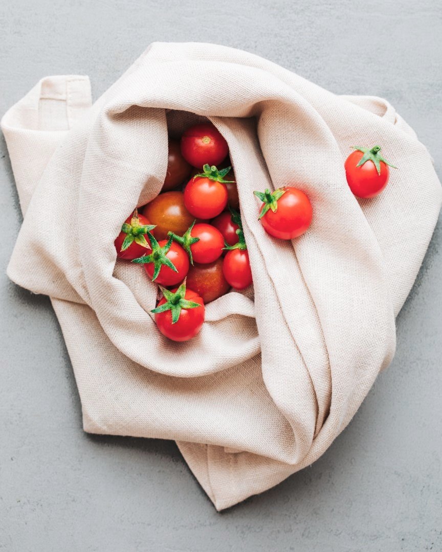Tomatoes inside a white cloth bag, with some spilling out onto a gray surface.