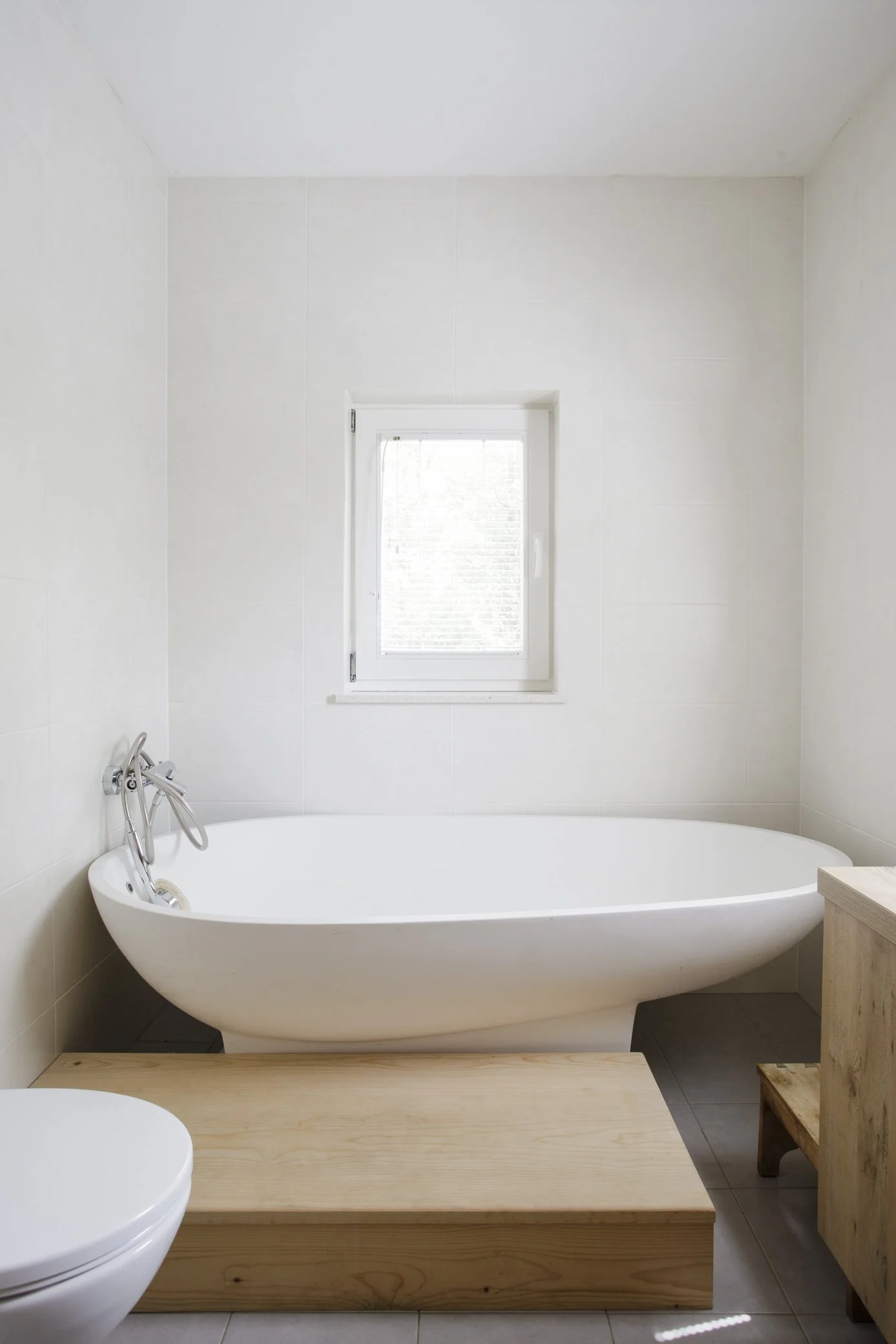 Minimalist bathroom with a white bathtub, a small window, and wooden furniture.