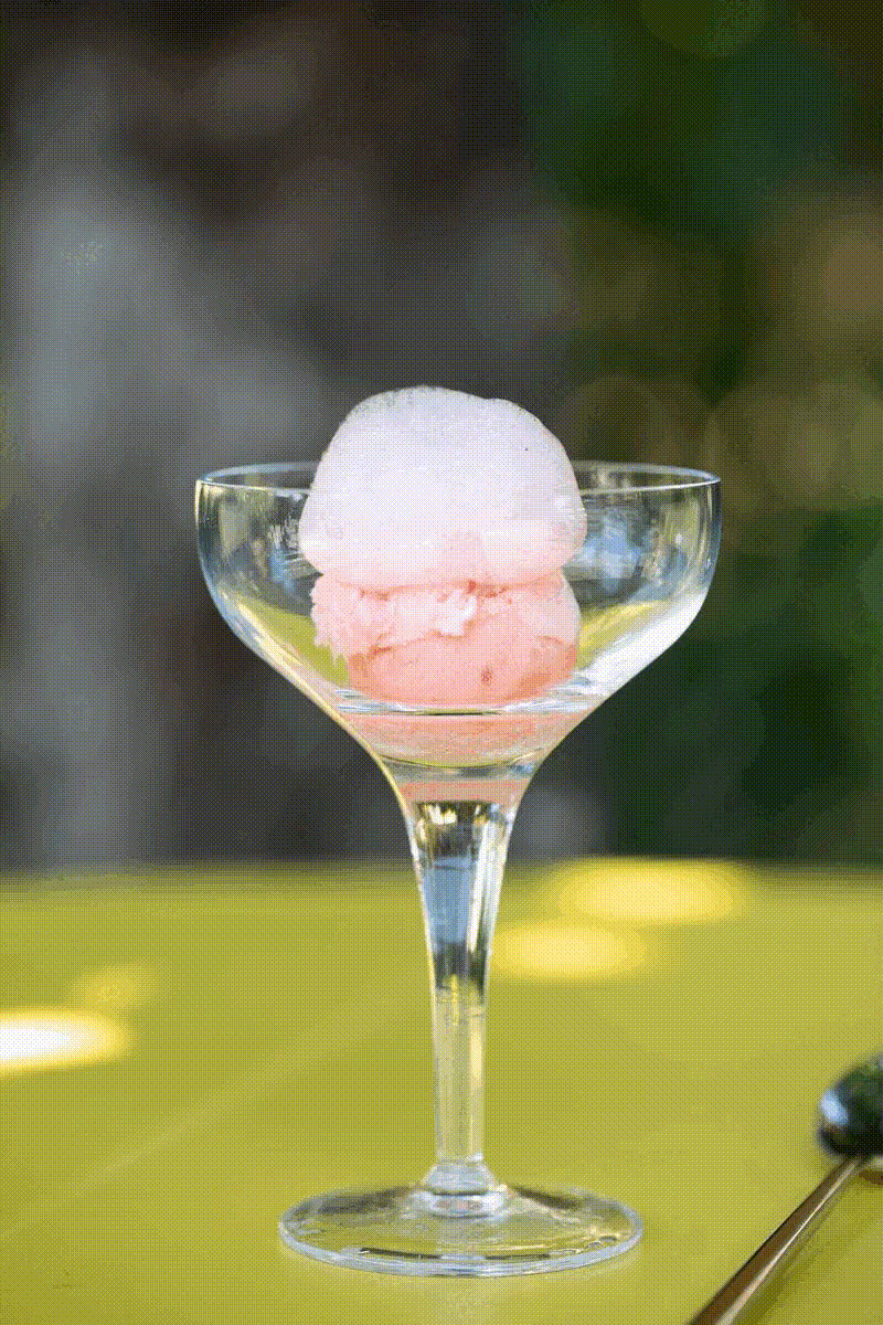 Two scoops of pink and white ice cream in a stemmed glass dish on a yellow surface