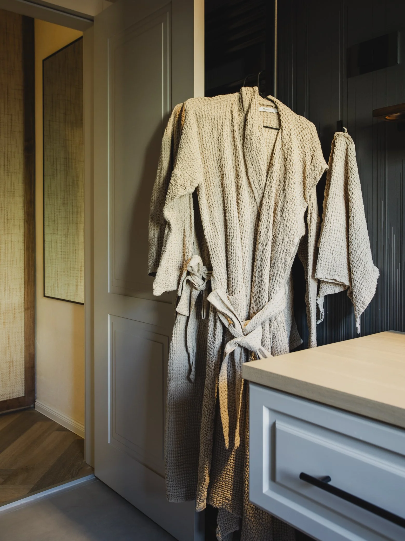 Cream-colored bathrobe hanging on the side of a black cupboard in a modern kitchen.