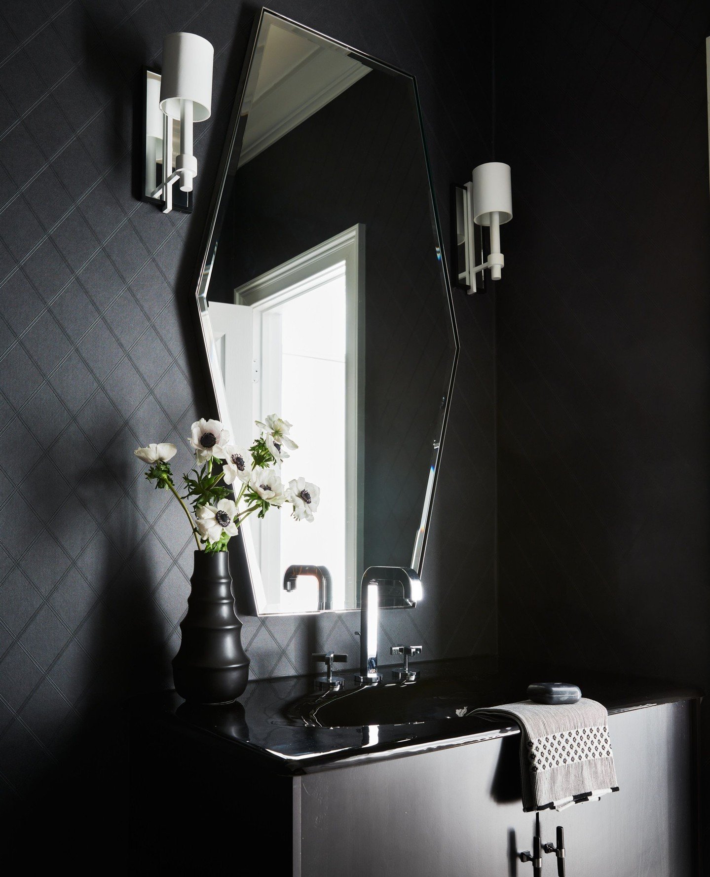We believe small spaces hold remarkable potential and provide the perfect chance to go bold. This powder room's black tone-on-tone wall covering, with its striking geometric pattern, enhances the room&rsquo;s depth while mirrored surfaces reflect lig
