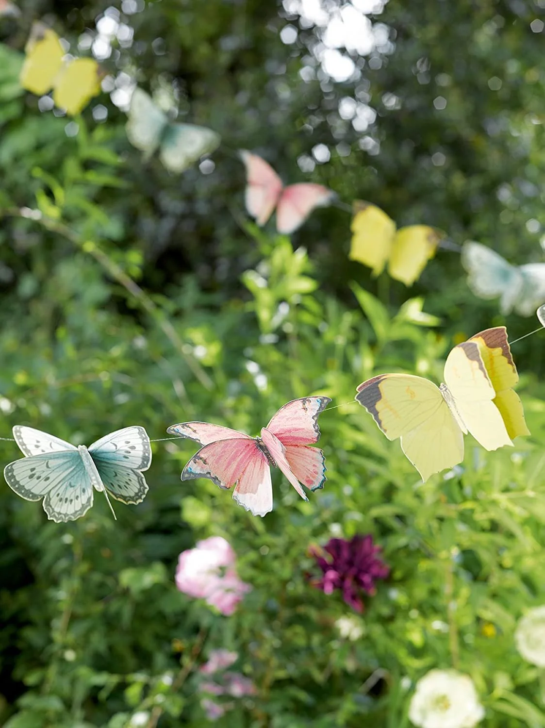 In the background, leafy green bushes and trees. In the foreground, bunting made of yellow, pink, and blue paper butterflies.