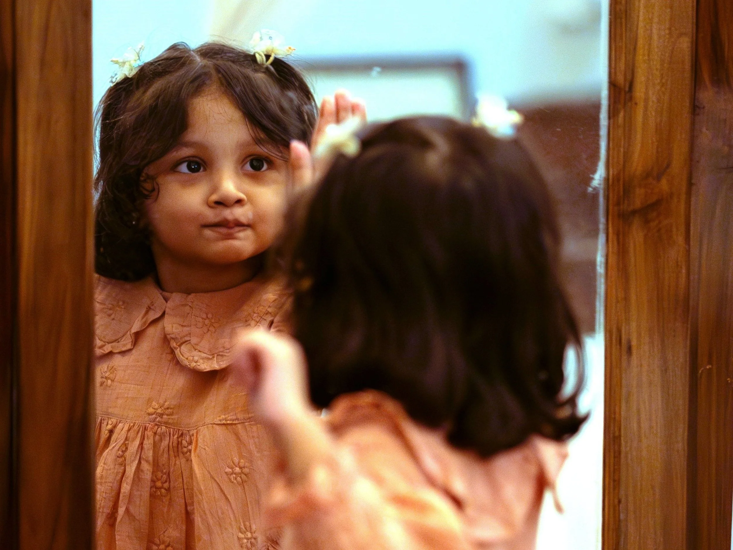 A child looks at herself in the mirror while polishing it.