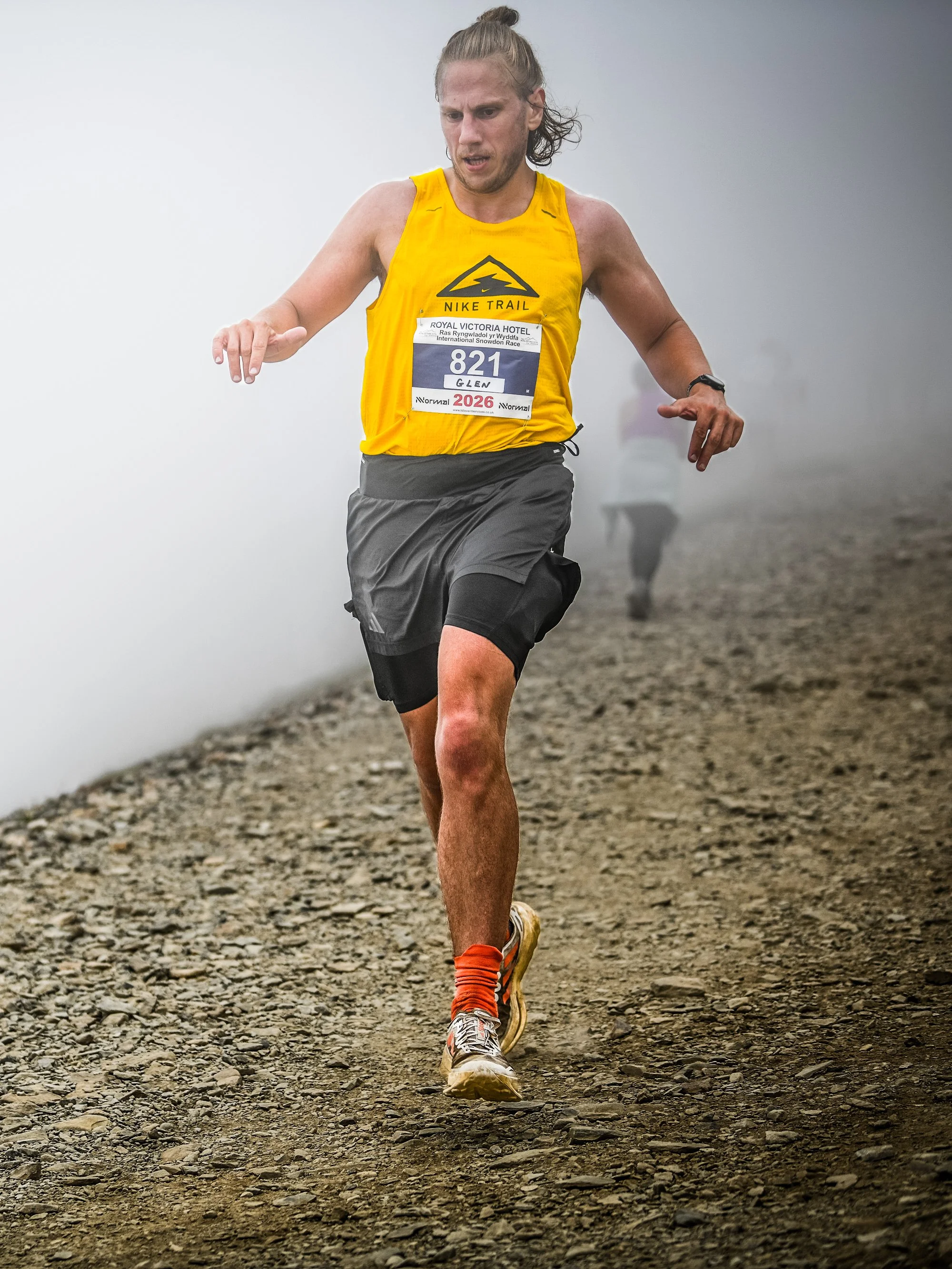 glen williams running during the snowdon race/ras yr wyddfa wearing a yellow nike vest with a race bib and black shorts running on a rocky trail in foggy weather.