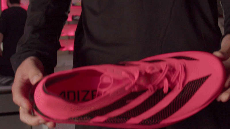 Person holding a pink and black athletic shoe with the brand name 'adizero' visible inside.