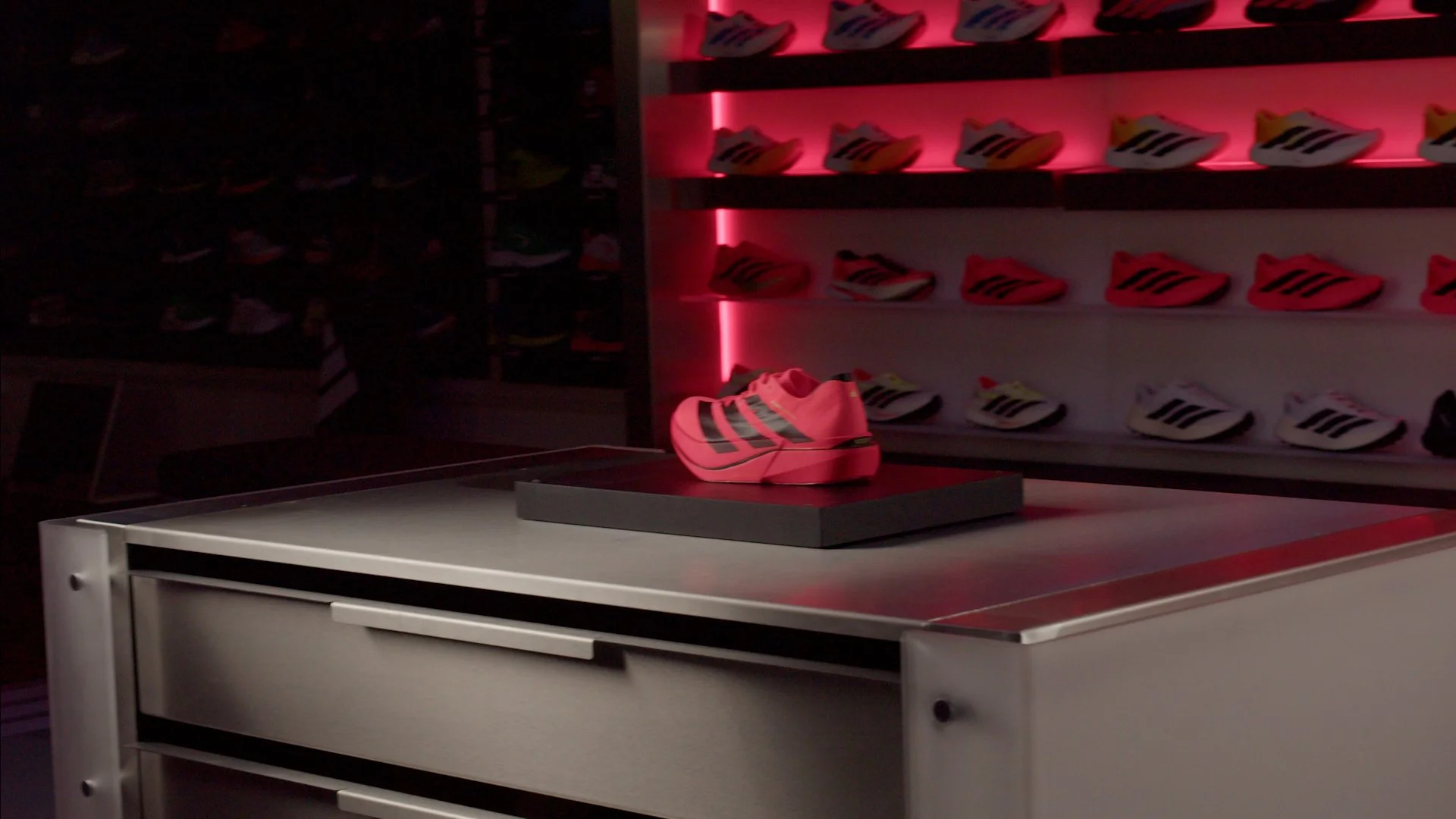 Display of colorful athletic shoes on shelves in a store with red lighting and a workspace counter in foreground.
