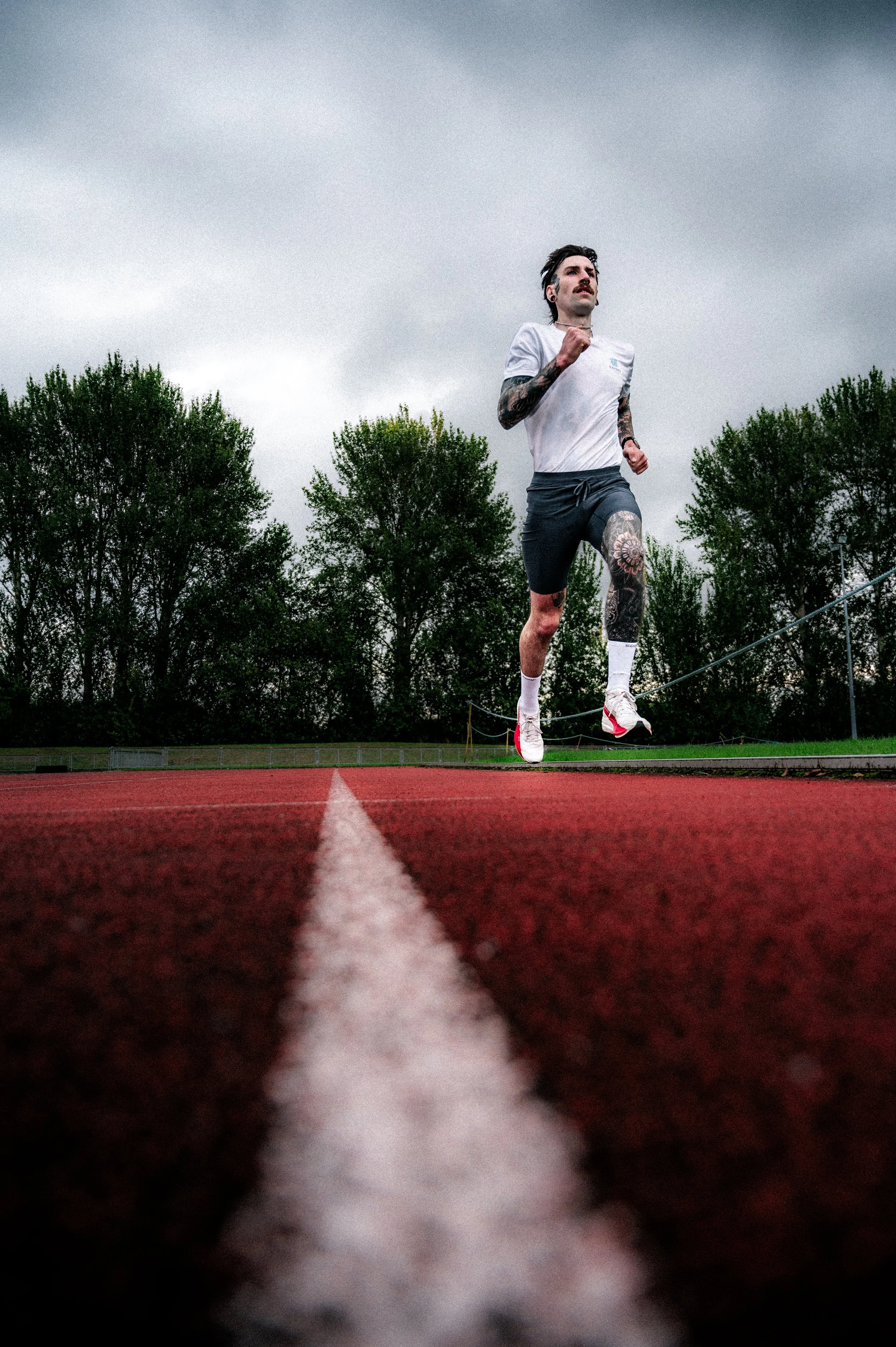 A man with tattoos running on a track field under a cloudy sky.