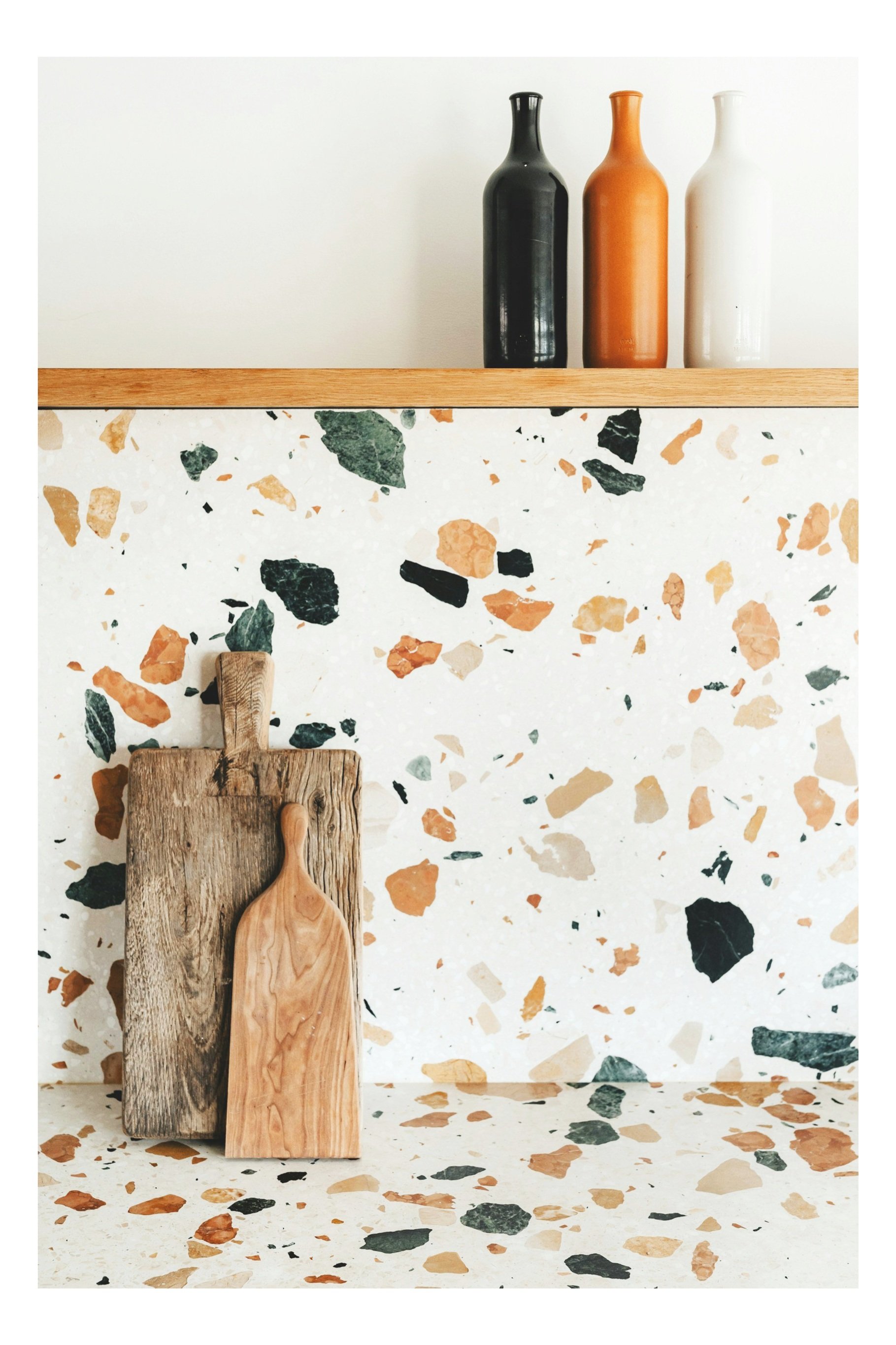 Decorative kitchen shelf with ceramic vases, wood cutting boards, and terrazzo wall and countertop design.