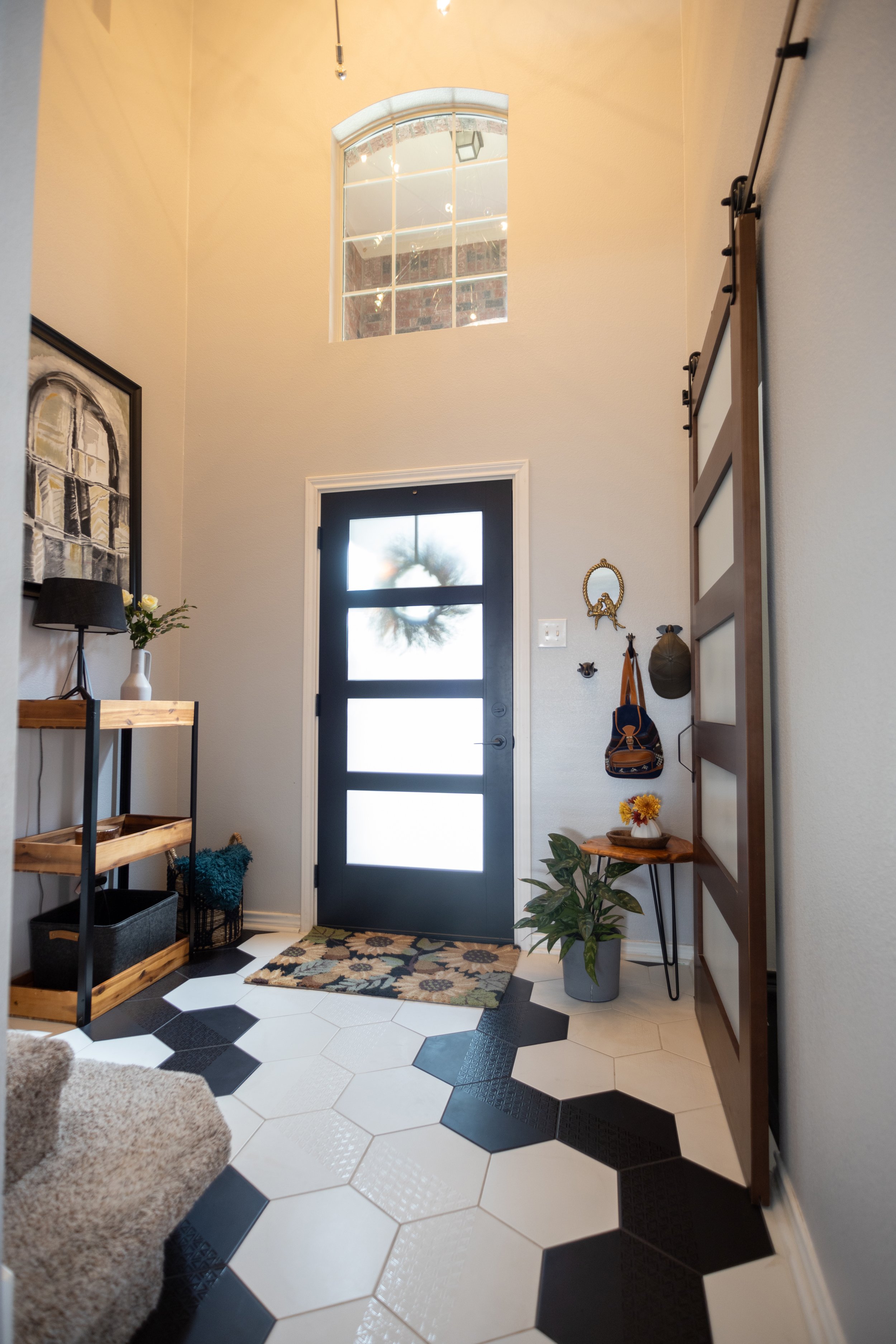 Foyer with black front door, decorative wreath, hallway with plants, and wall-mounted sliding barn door.