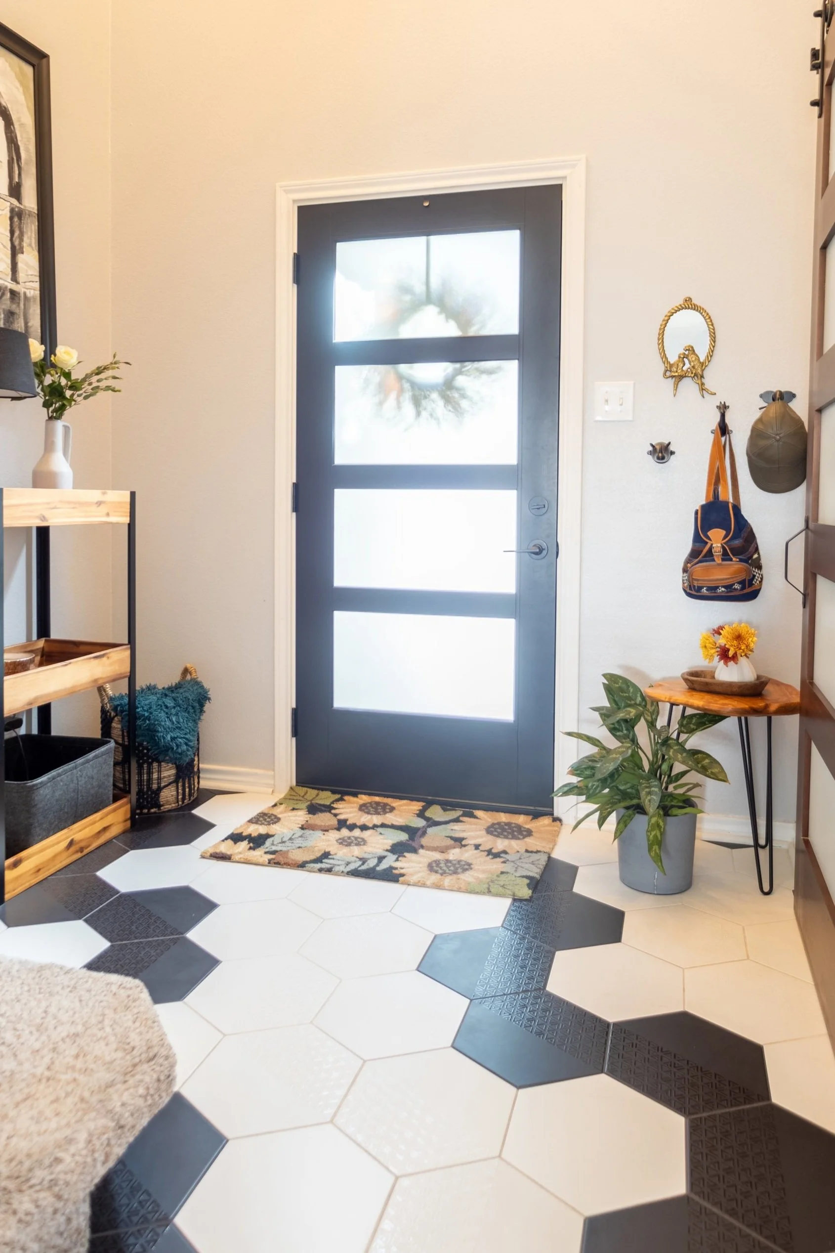 Stylish entryway with black front door, floral doormat, side table with flowers, coat hooks, and decorative shelving.
