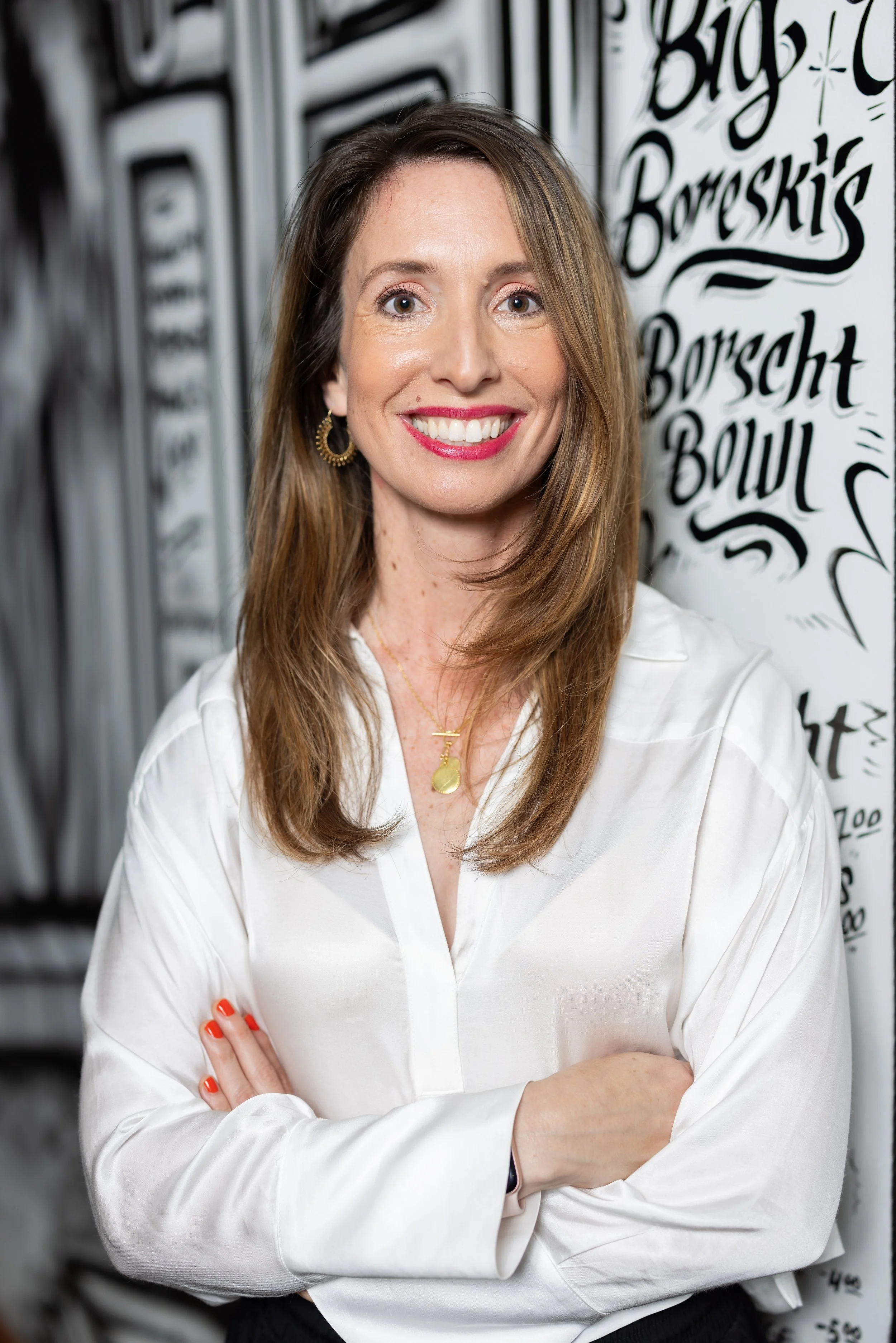 Interior designer Naomi smiling with arms crossed in front of a black and white handwritten mural