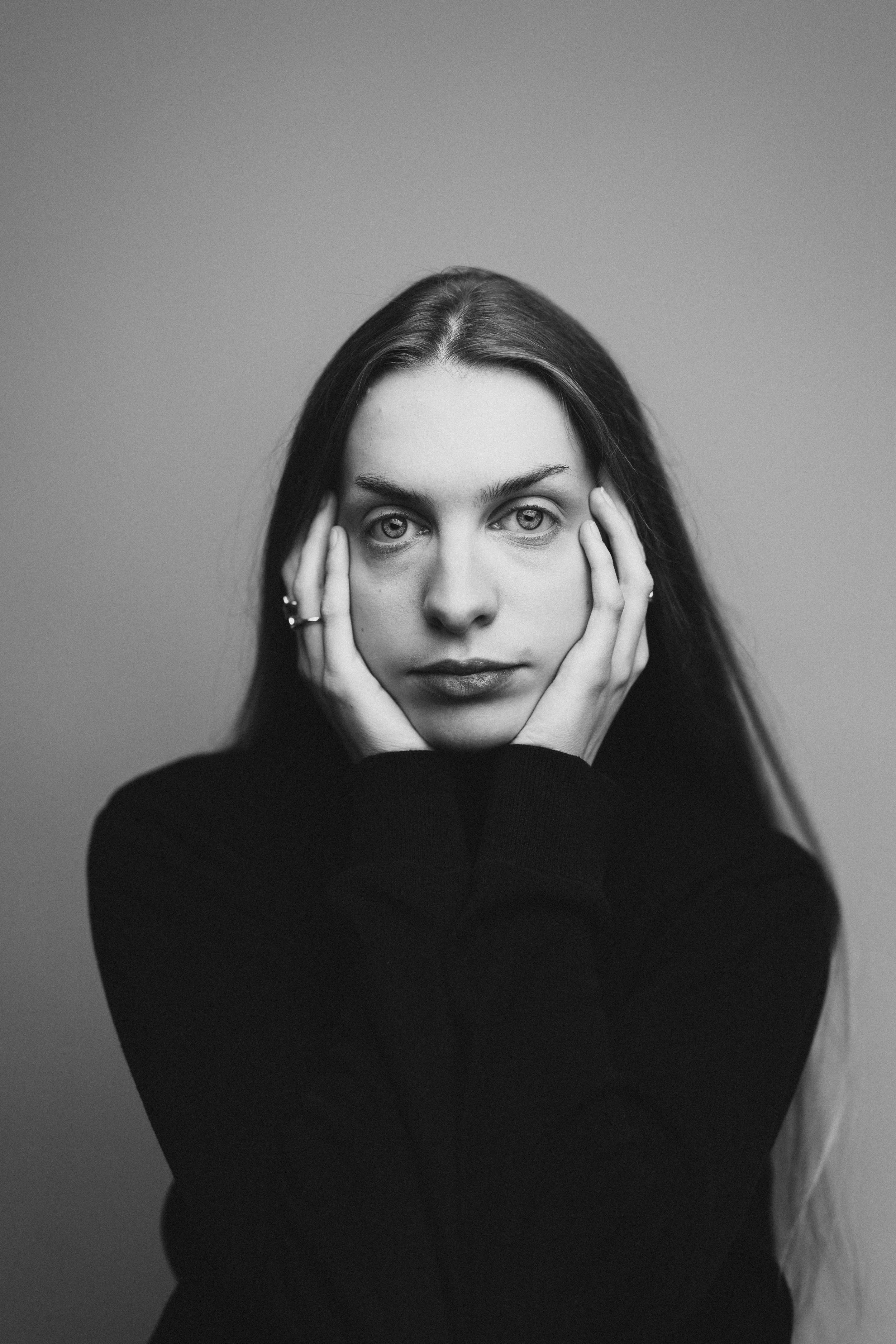 Schwarz-weiß-Fotografie einer jungen Frau mit langen Haaren, die ihre Hände am Kopf hält.