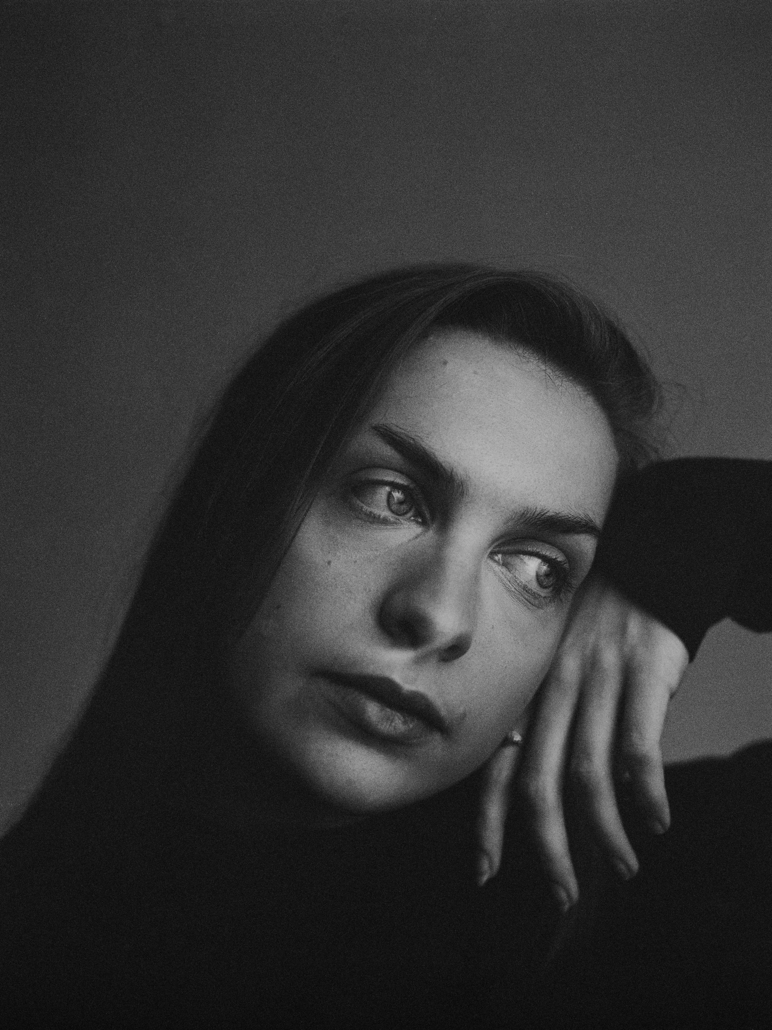 Schwarz-Weiß-Porträt einer jungen Frau mit langen Haaren, die nachdenklich aussieht, mit Blick zur Seite, die Hand an das Gesicht gelegt