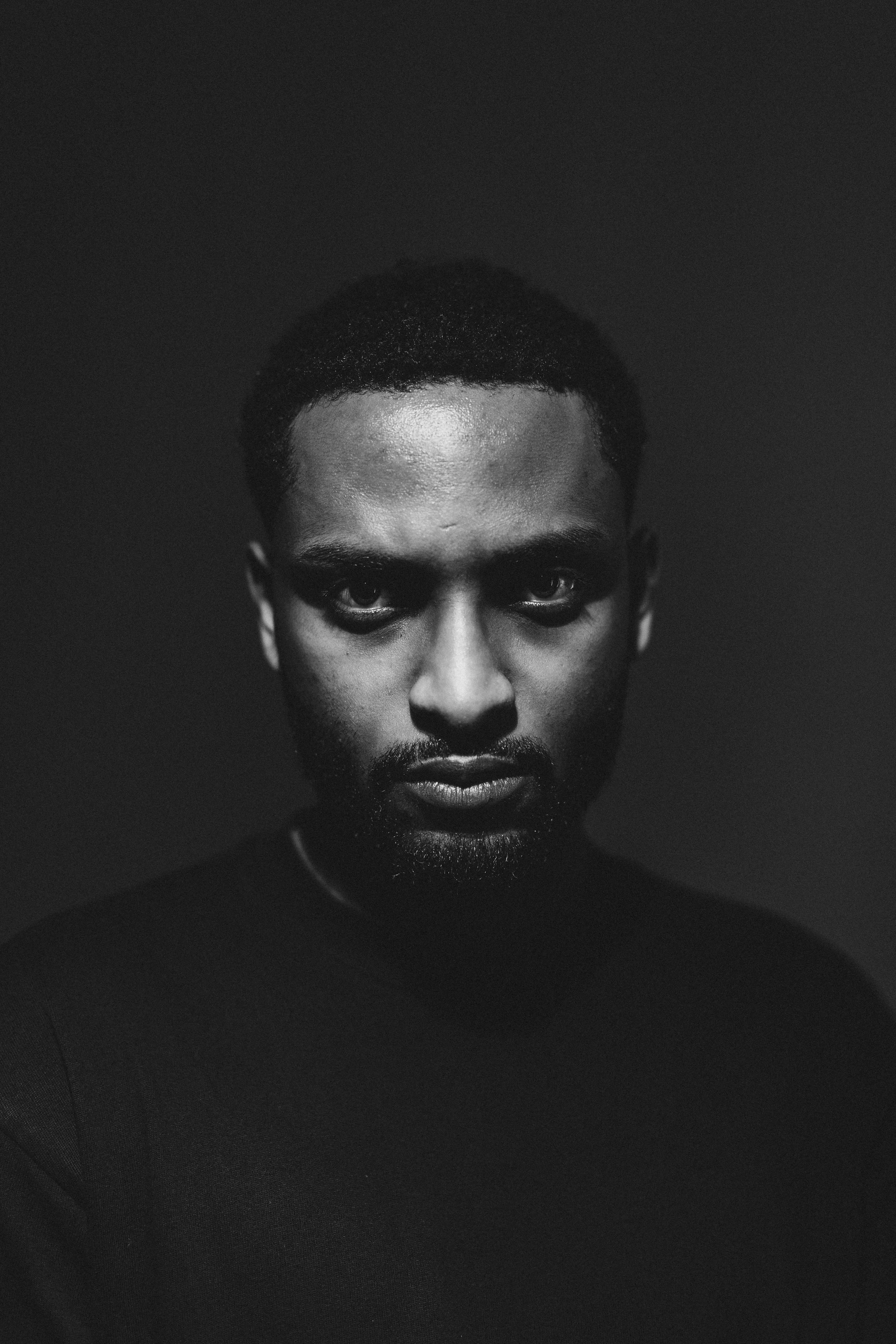 Schwarz-Weiß-Porträt eines schwarzen Mannes mit kurzen Haaren und Bart, blickt ernst in die Kamera.