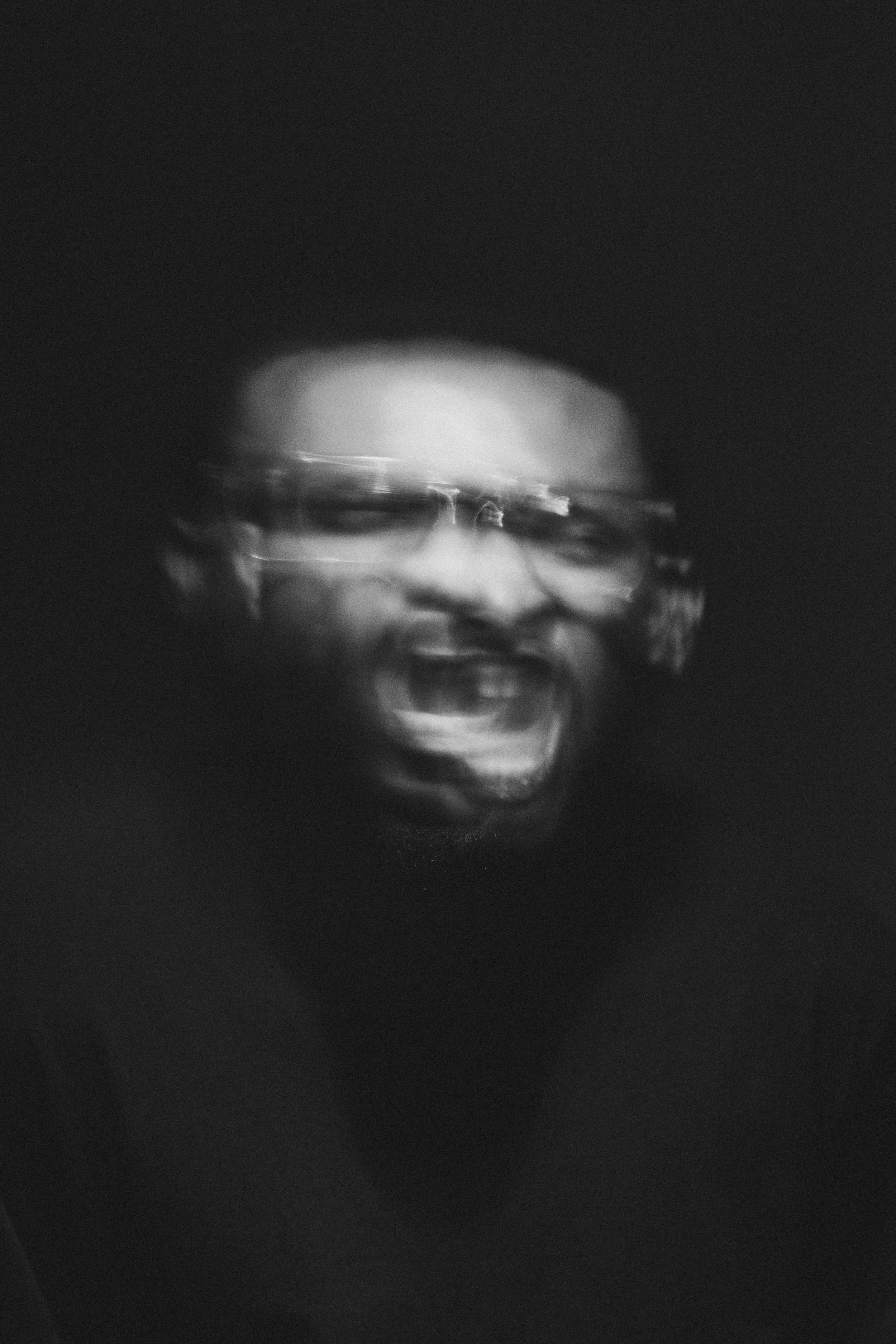 Schwarzes und weißes Bild eines schreienden Mannes mit Brille, unscharf und mit Bewegungseffekt.