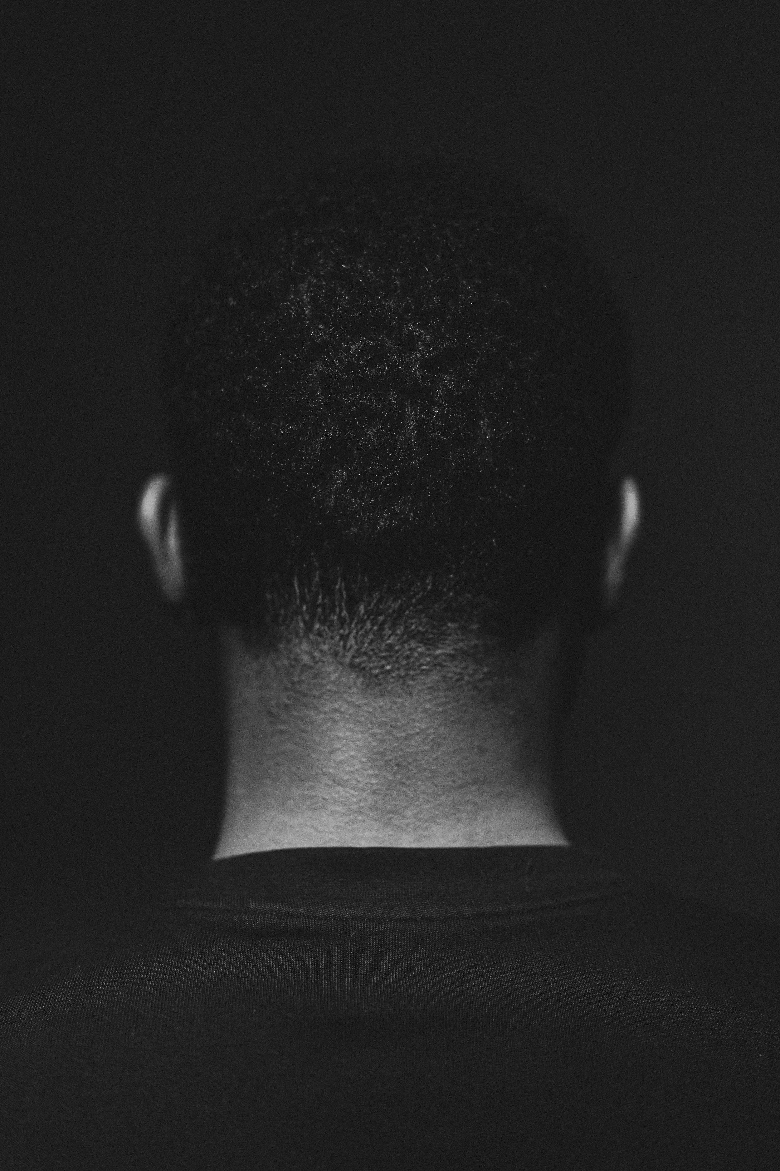 Schwarze, kurze Haarfrisur, Nahaufnahme des Hinterkopfs einer schwarzen Person, gegen einen schwarzen Hintergrund.