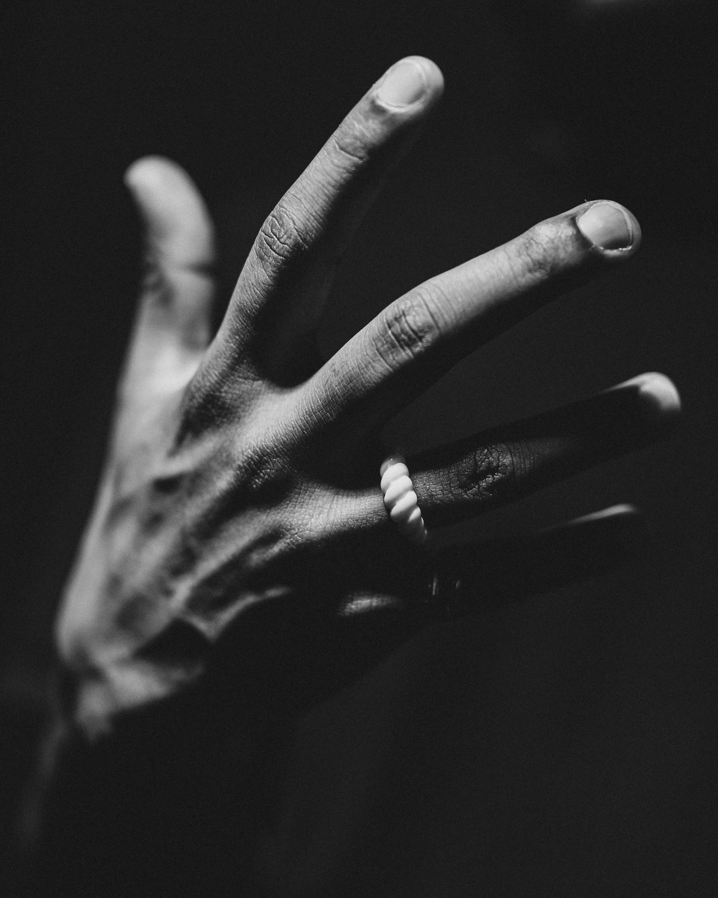 Schwarz-weiß-Foto einer Hand mit einem Ring und einem kleinen Gegenstand an einem Finger.