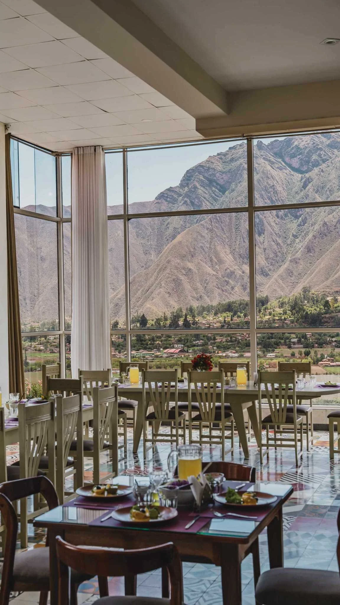 A restaurant dining area with tables set for a meal, large windows showing mountain scenery, and a colorful patterned tile floor.