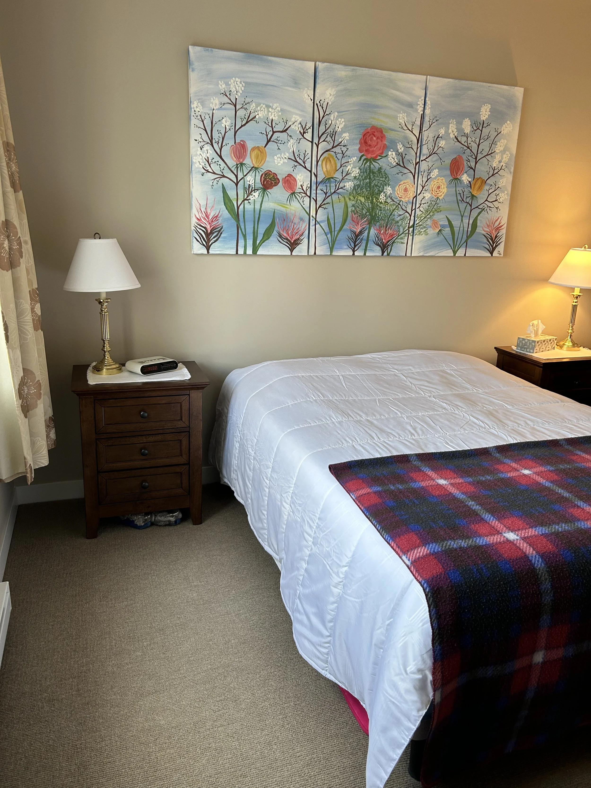 A cozy bedroom with a bed, nightstands on each side, and a colorful floral painting above the bed.