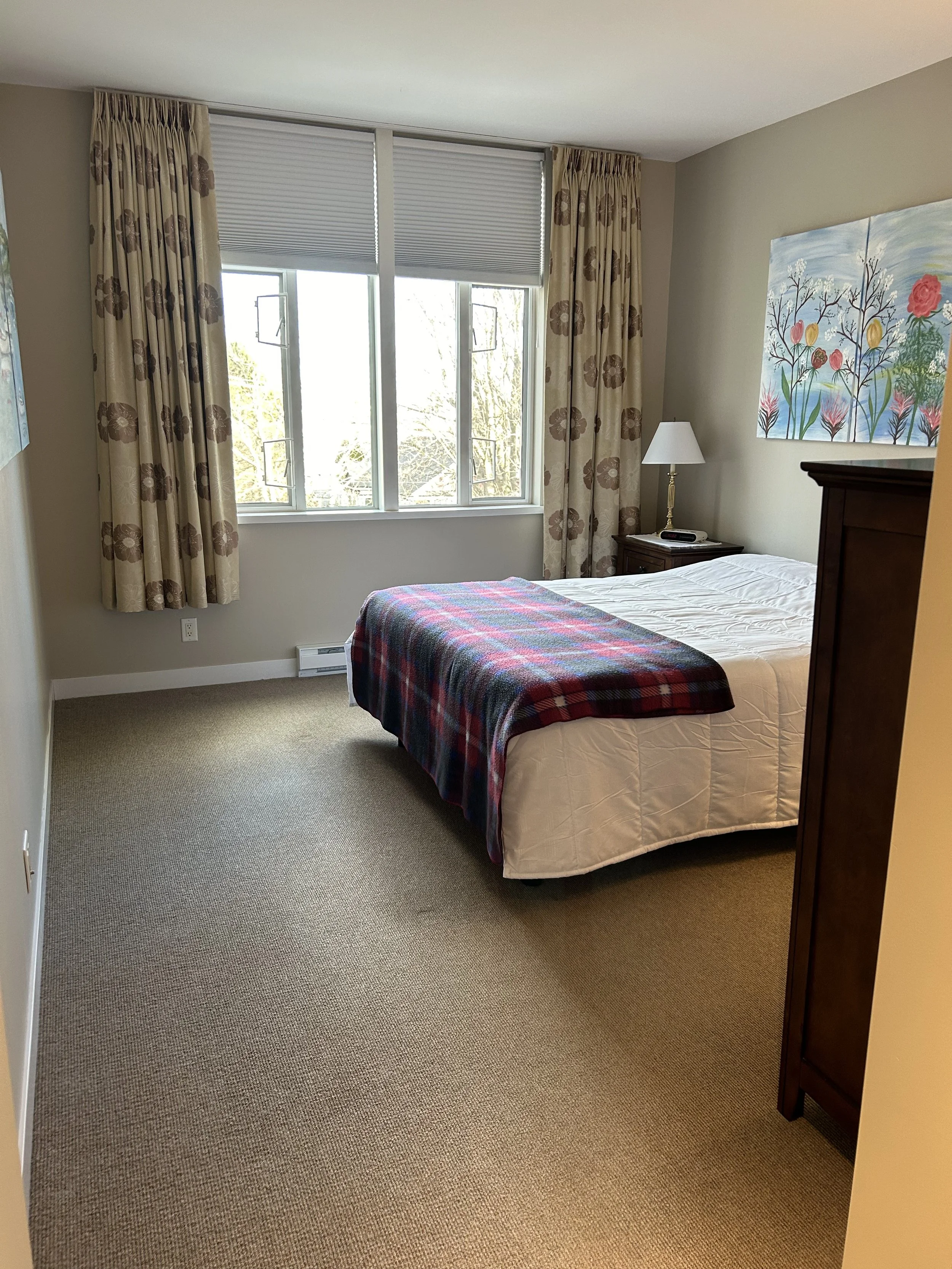 A bedroom with a bed, nightstand, lamp, and window with curtains and blinds.