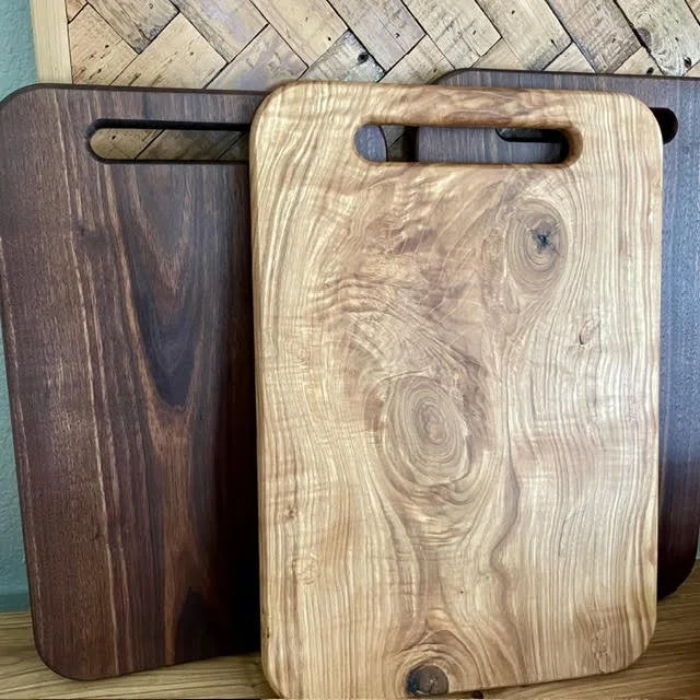 handcrafted-hardwood-cutting-boards-natuThree handcrafted rectangular hardwood cutting boards with cutout handles, featuring contrasting wood tones and natural grain patterns.ral-wood-grain.jpg