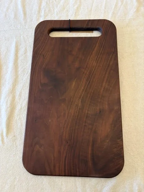 Rectangular dark walnut cutting board with rounded corners, a cutout carrying handle, and rich natural wood grain.
