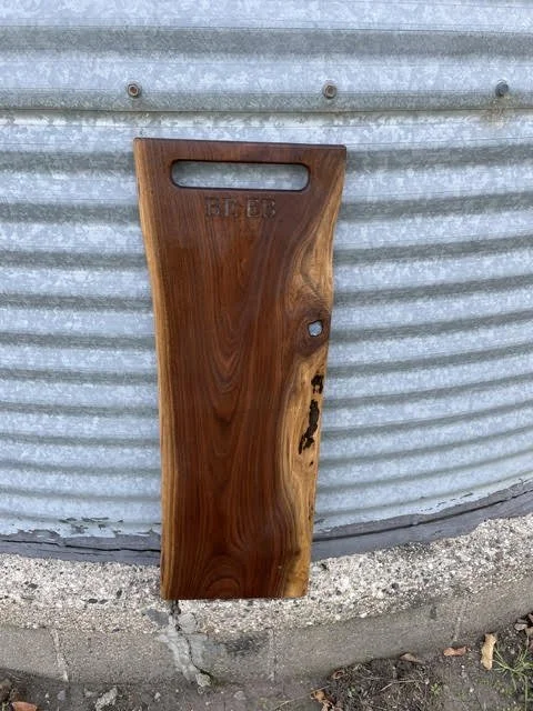 Handcrafted dark hardwood cutting board with a cutout handle, natural wood grain, and rustic live-edge detail.